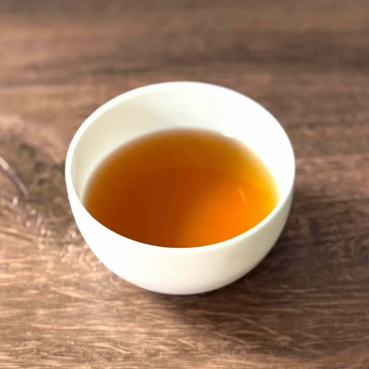 a white bowl of dark oolong tea on a wood table