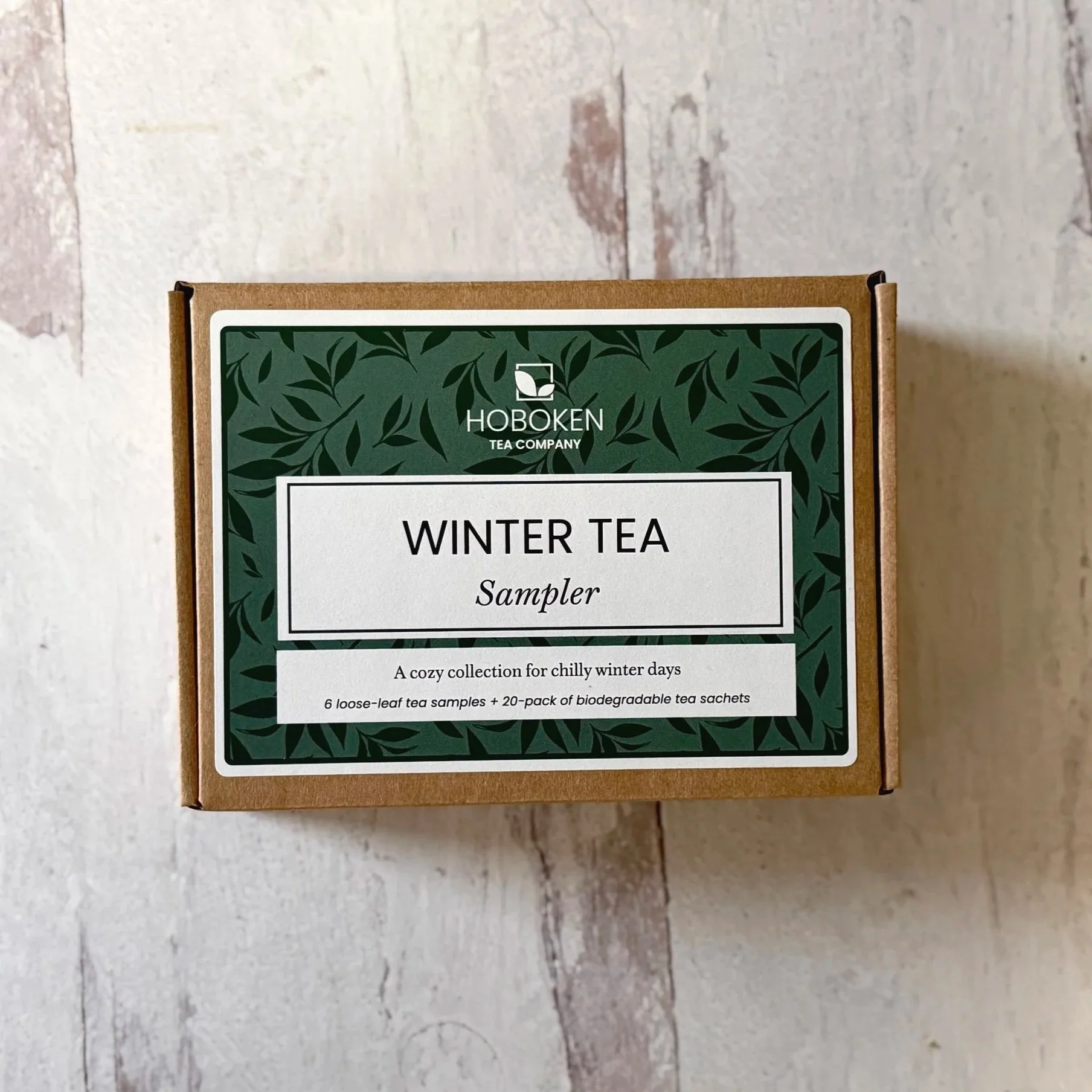 A box labeled Winter Tea Sampler from Hoboken Tea Company on a light wood surface