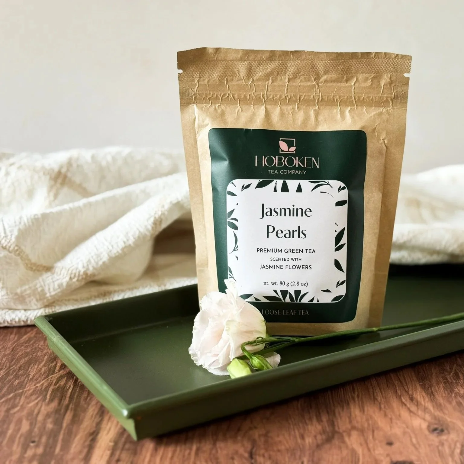 a package of Jasmine Pearls loose leaf green tea from Hoboken Tea Company on a tray with flowers