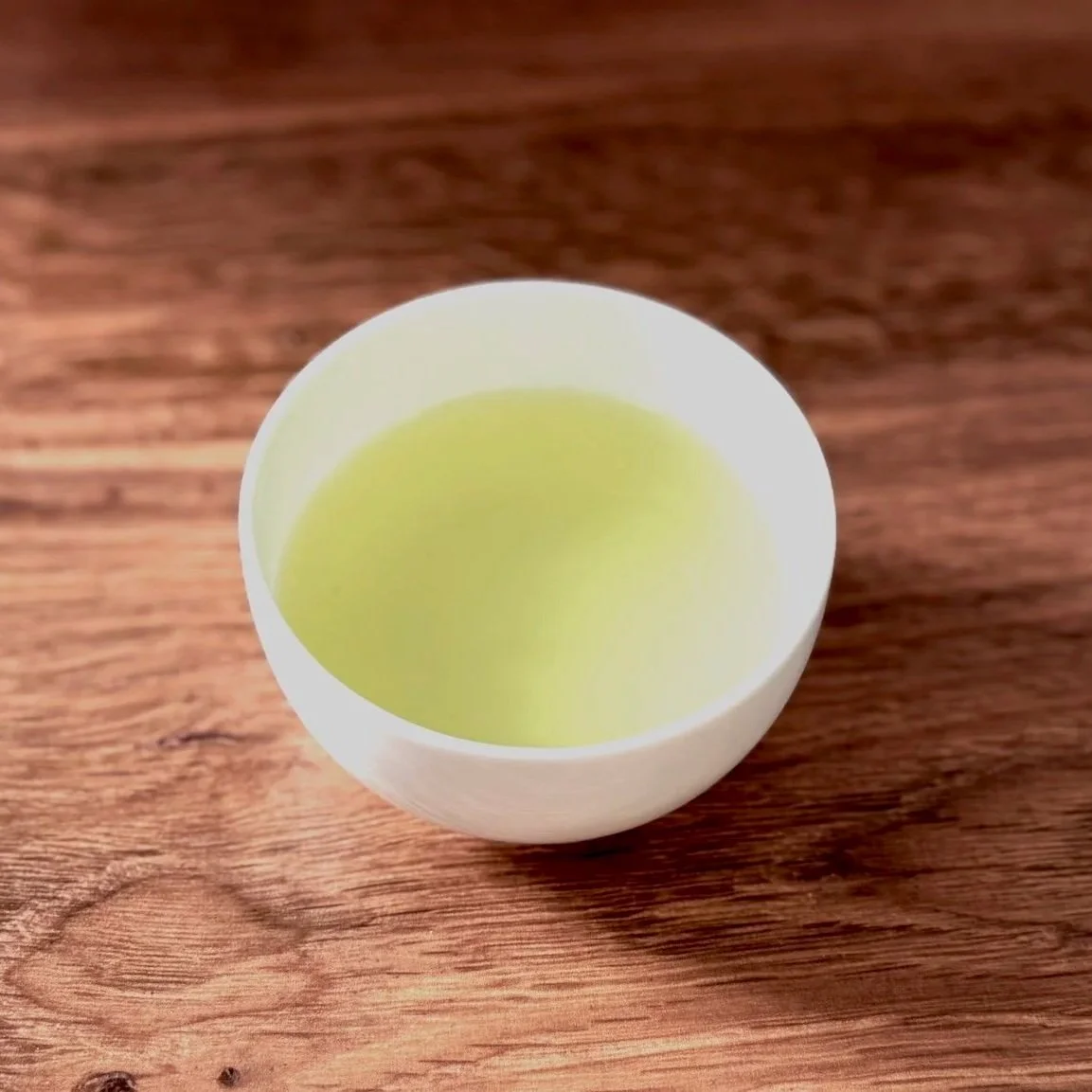 a white bowl of green tea on a wood table