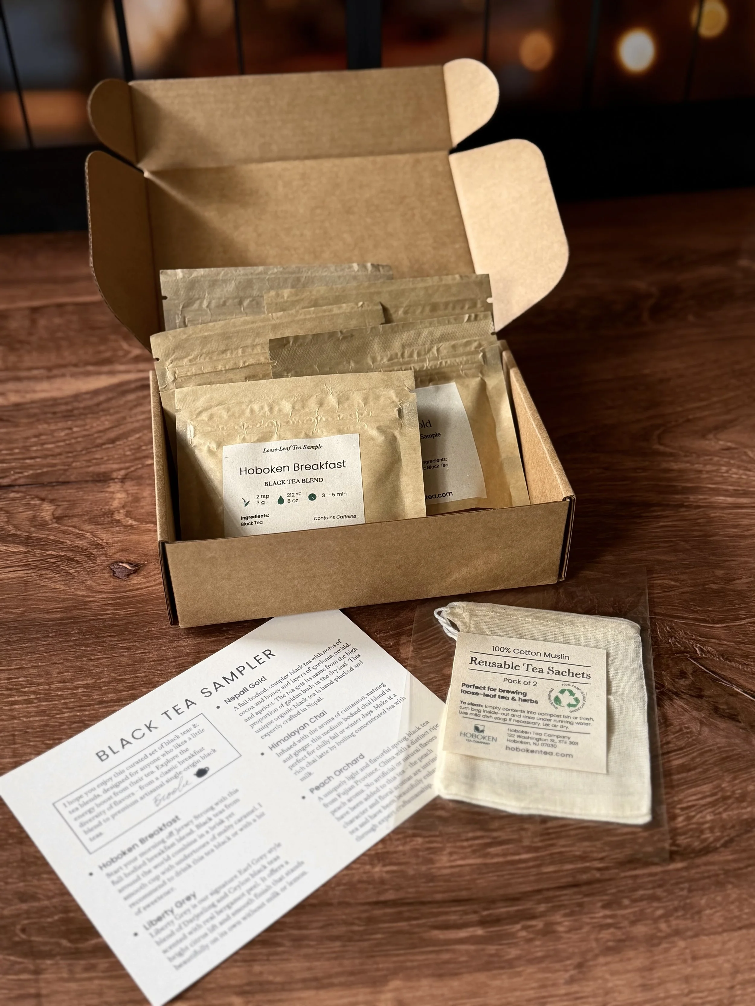 an open box containing several small packets of loose leaf tea on a table next to cotton tea bags and an info card