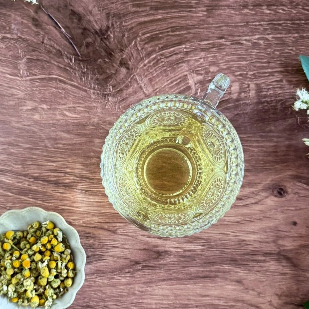 a cup of chamomile tea next to a dish of dried organic chamomile flowers