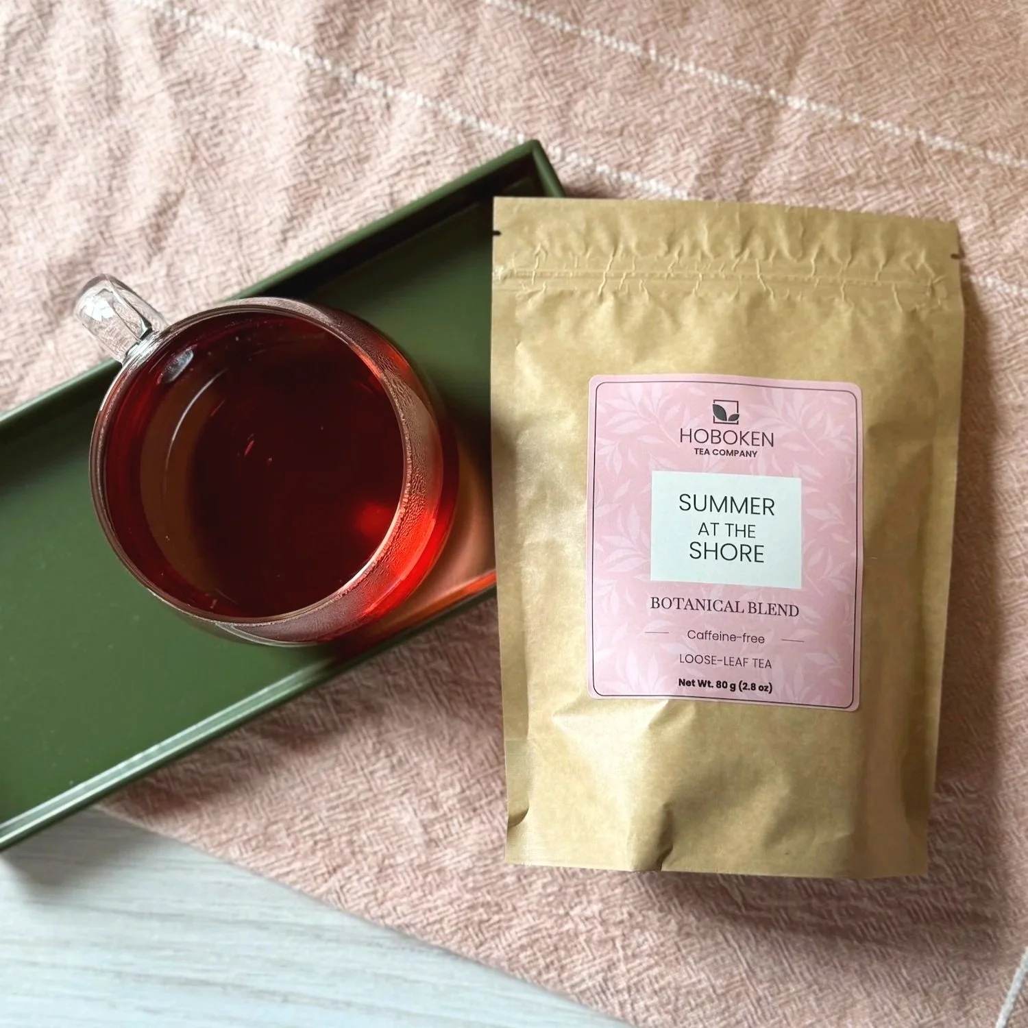 a packet of Summer on the Shore herbal tea on a tray next to a cup of hibiscus mint tea