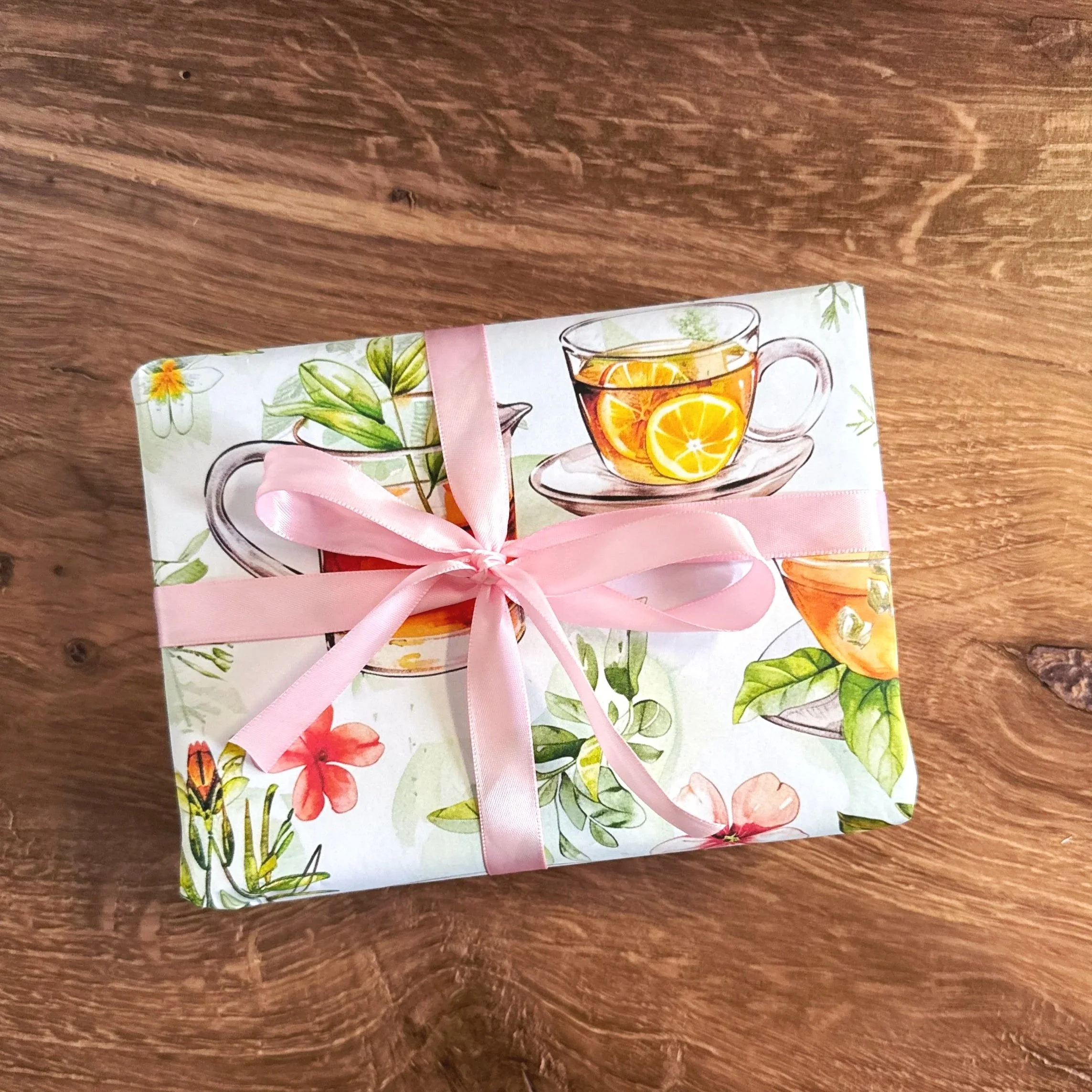 a package wrapped in floral teacups pattern wrapping paper with a pink ribbon on a wood table