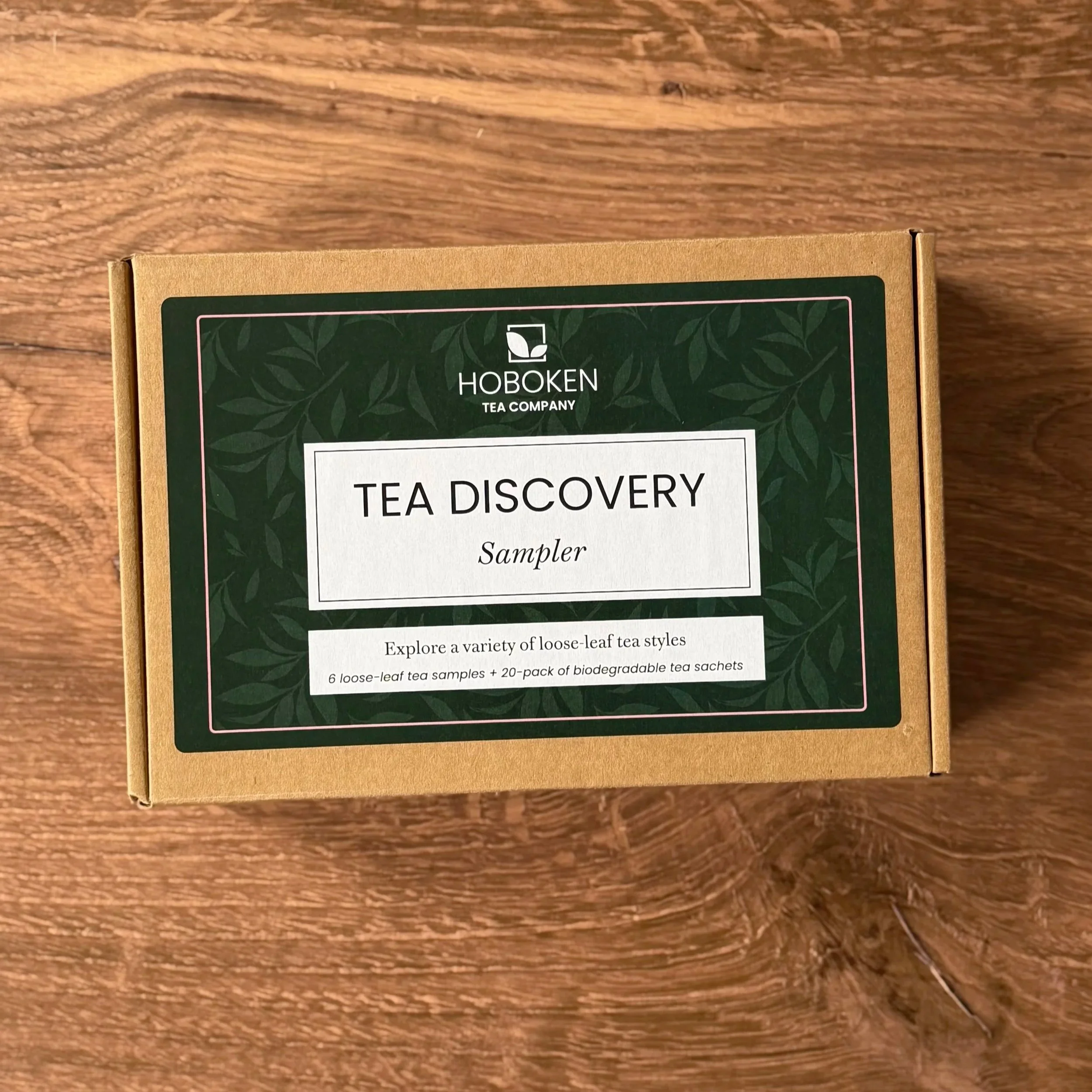 A small box with a green Hoboken Tea Company label reading "Tea Discovery Sampler"  on a wood table