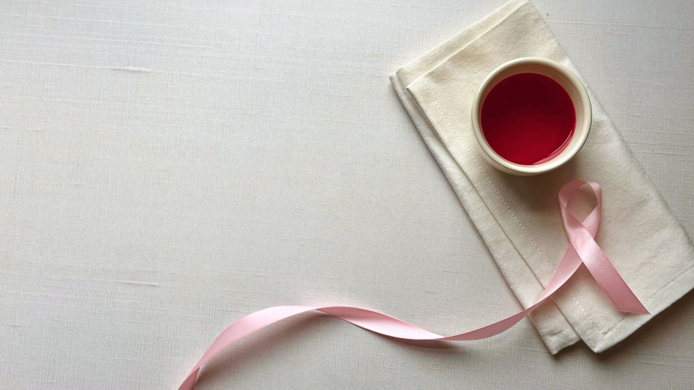 a cup of red tea on a cloth napkin next to a pink ribbon for breast cancer awareness