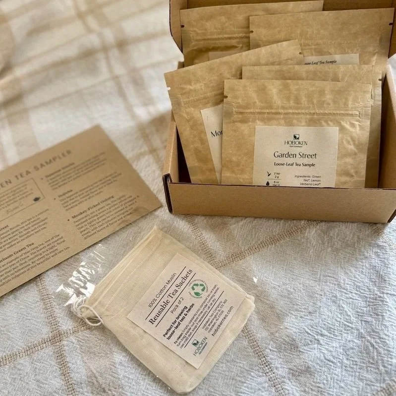 an open loose leaf tea sampler box next to a notecard and a pack of reusable cotton tea bags