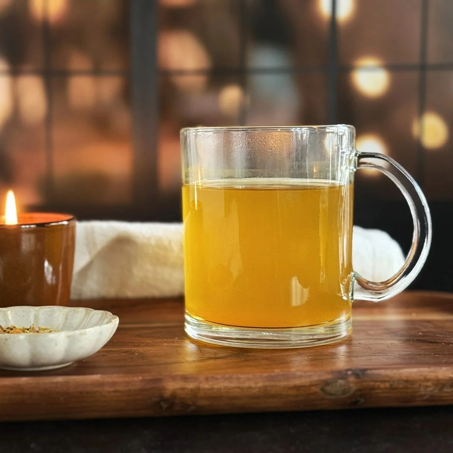 a glass mug of yellow herbal turmeric ginger tea next to a candle on a wooden table