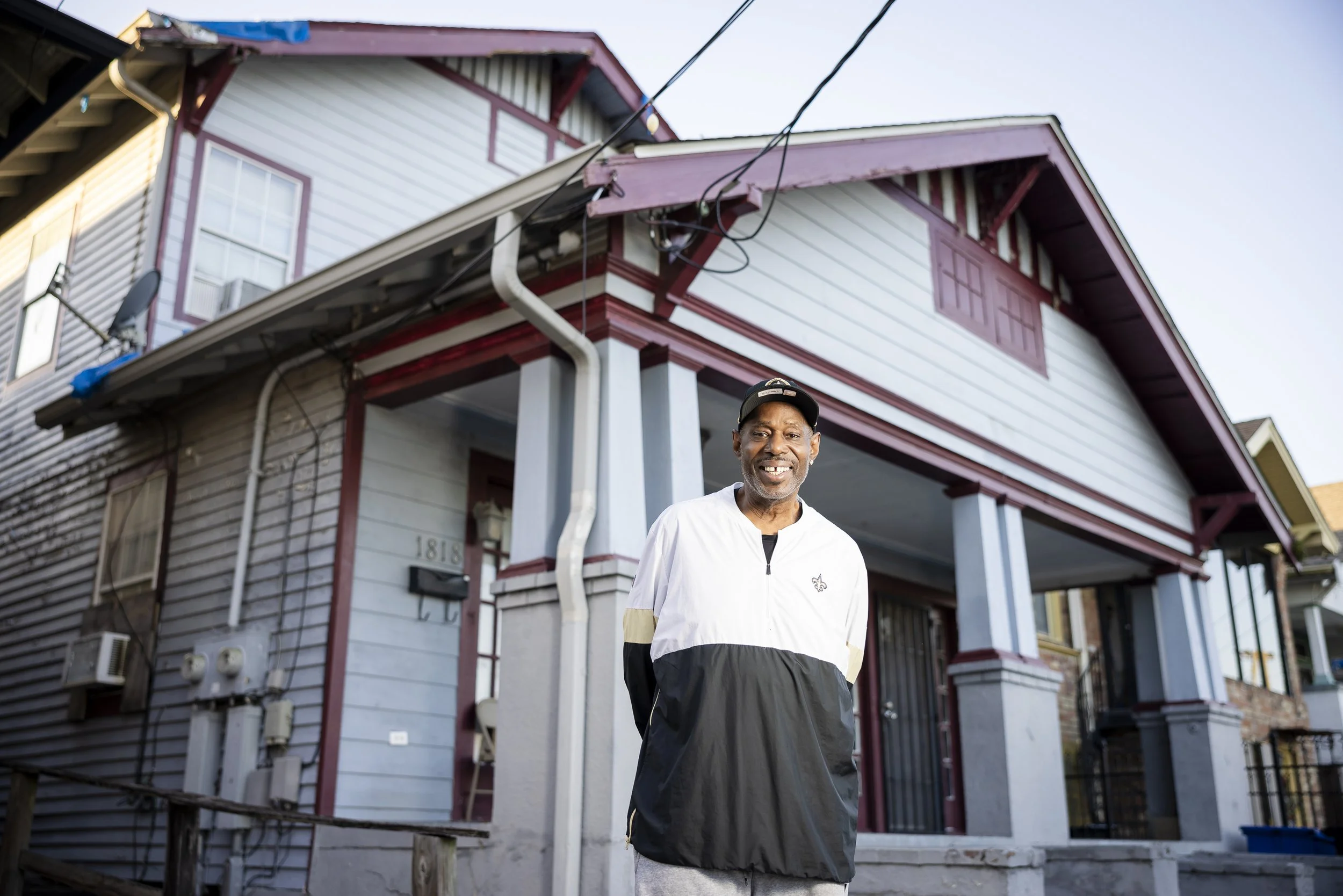 A man smiling standing in front of a two-story house with white and red exterior.