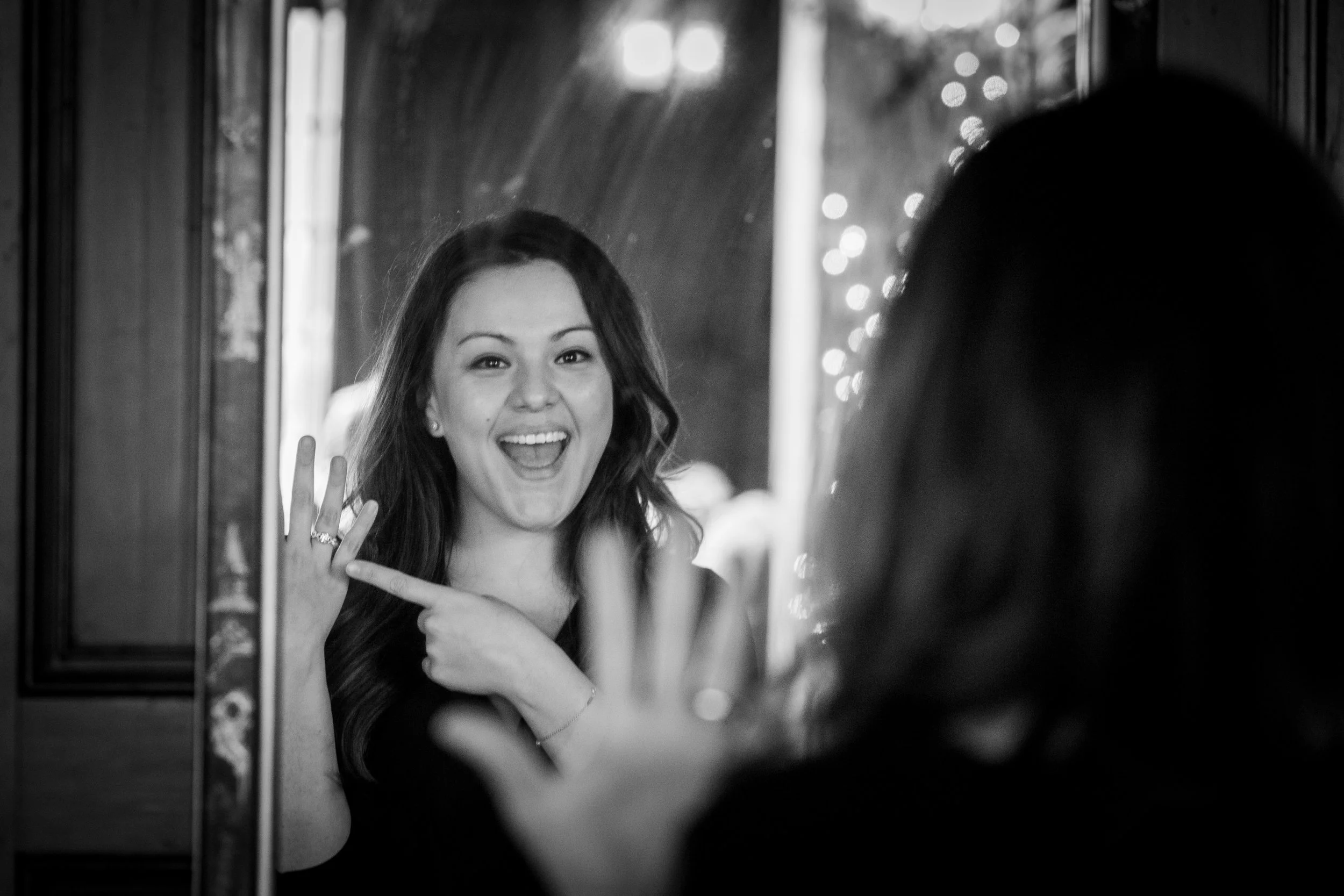 A woman looking at herself in a mirror, smiling and pointing at her reflection.