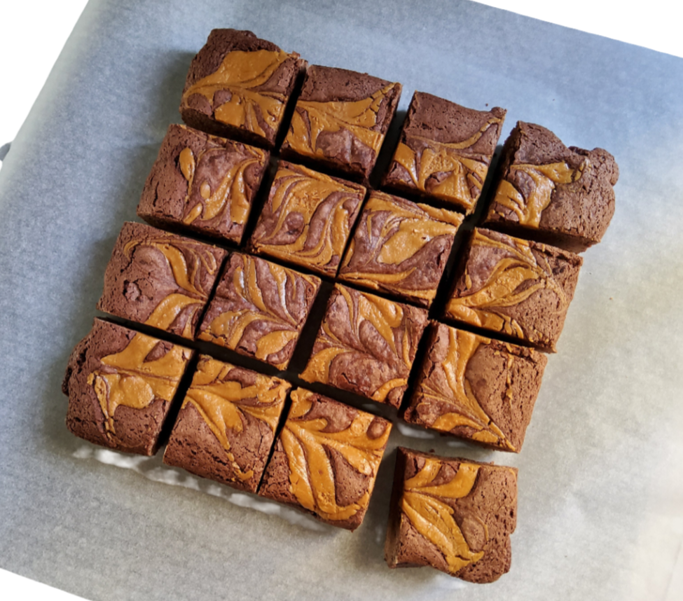 Top-down view of vegan chocolate brownies with peanut butter swirls, cut into 16 pieces on parchment paper.