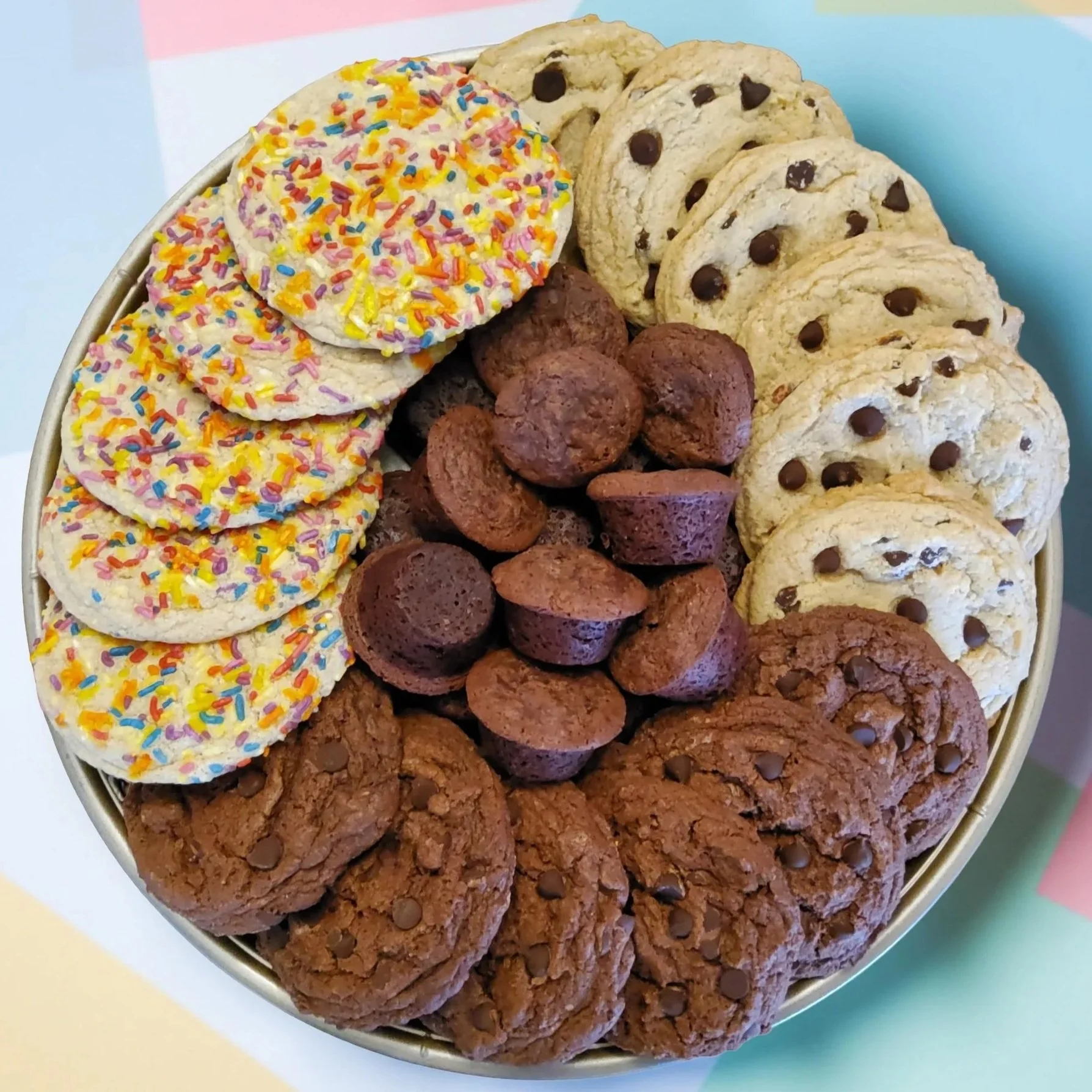 A platter filled with vegan chocolate chip cookies, sprinkled sugar cookies, double chocolate cookies, and brownie bites in the middle of them.