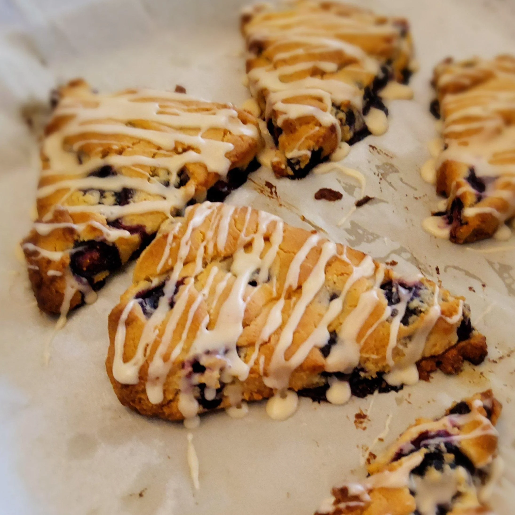 Vegan and gluten-free blueberry scones drizzled with white glaze on parchment paper