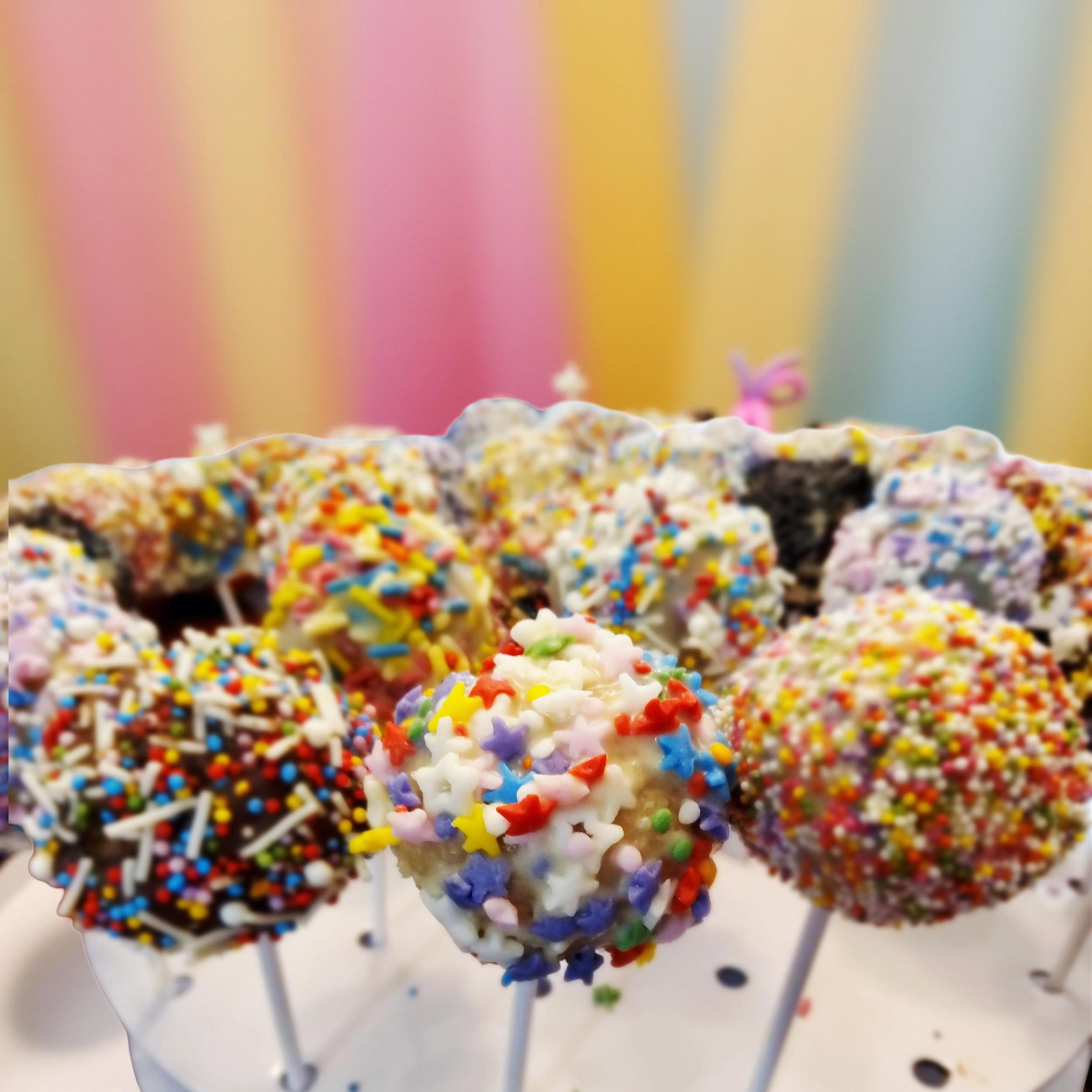 Assorted vegan cake pops decorated with colorful sprinkles and frosting.