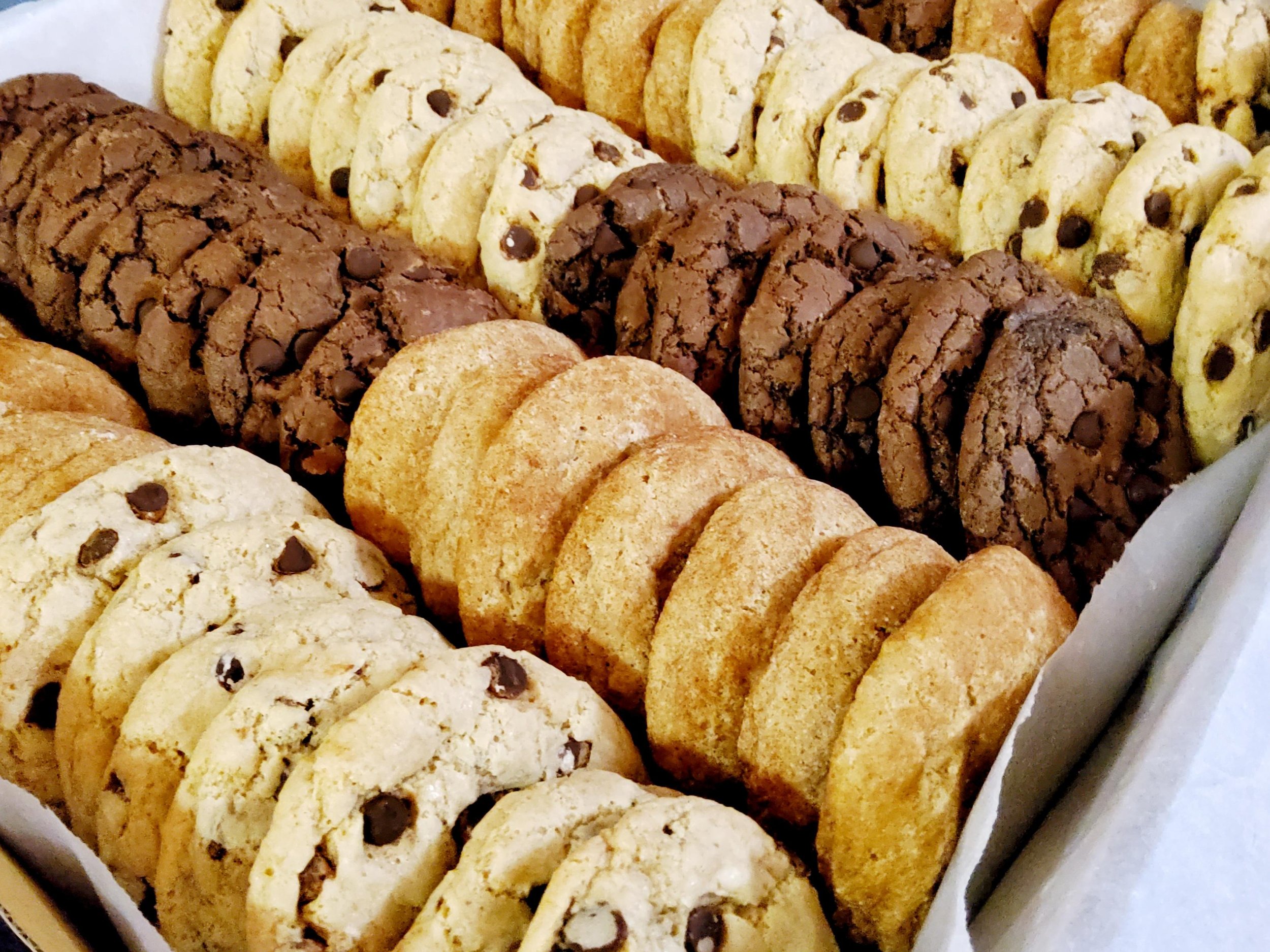Assorted vegan cookies including chocolate chip, cinnamon sugar, and double chocolate cookies in a box.