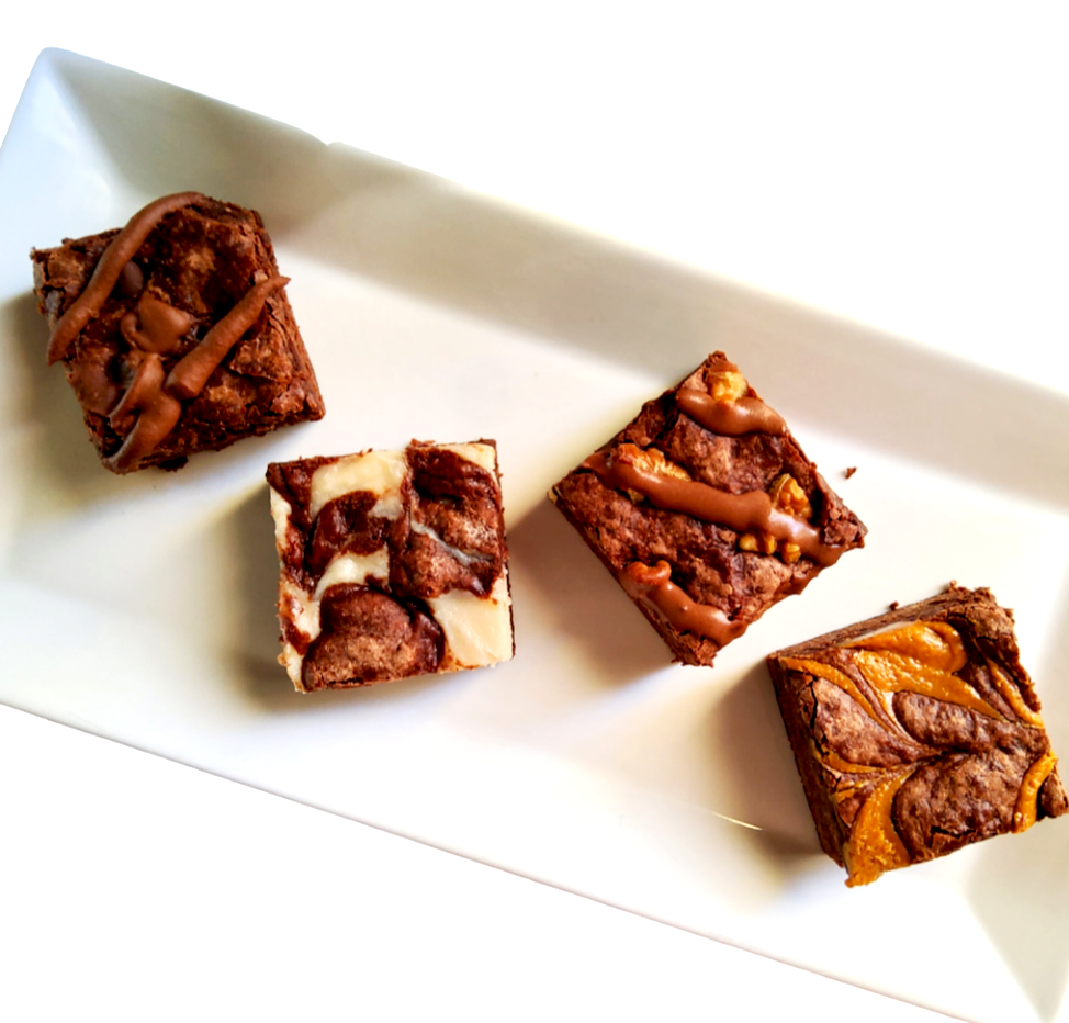 Four vegan brownies on a white rectangular plate, each with different toppings or mix-ins, including chocolate drizzles and swirls.