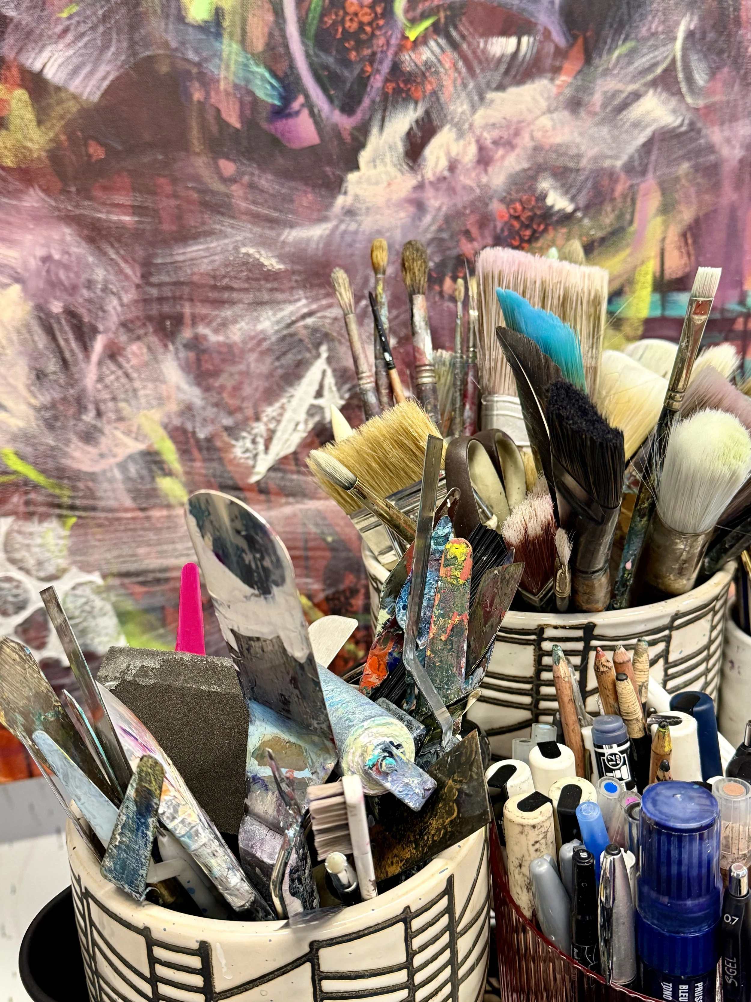 A container filled with various paintbrushes and art supplies, including bottles of paint and markers.