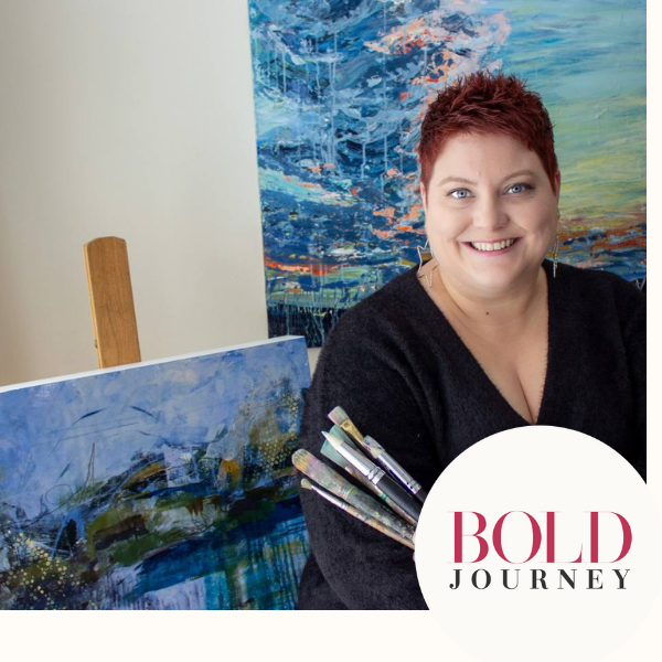 A smiling woman with short red hair sitting beside colorful abstract landscape paintings in an art studio or gallery. A white circle with the words 'BOLD JOURNEY' in pink and black is in the bottom right corner.
