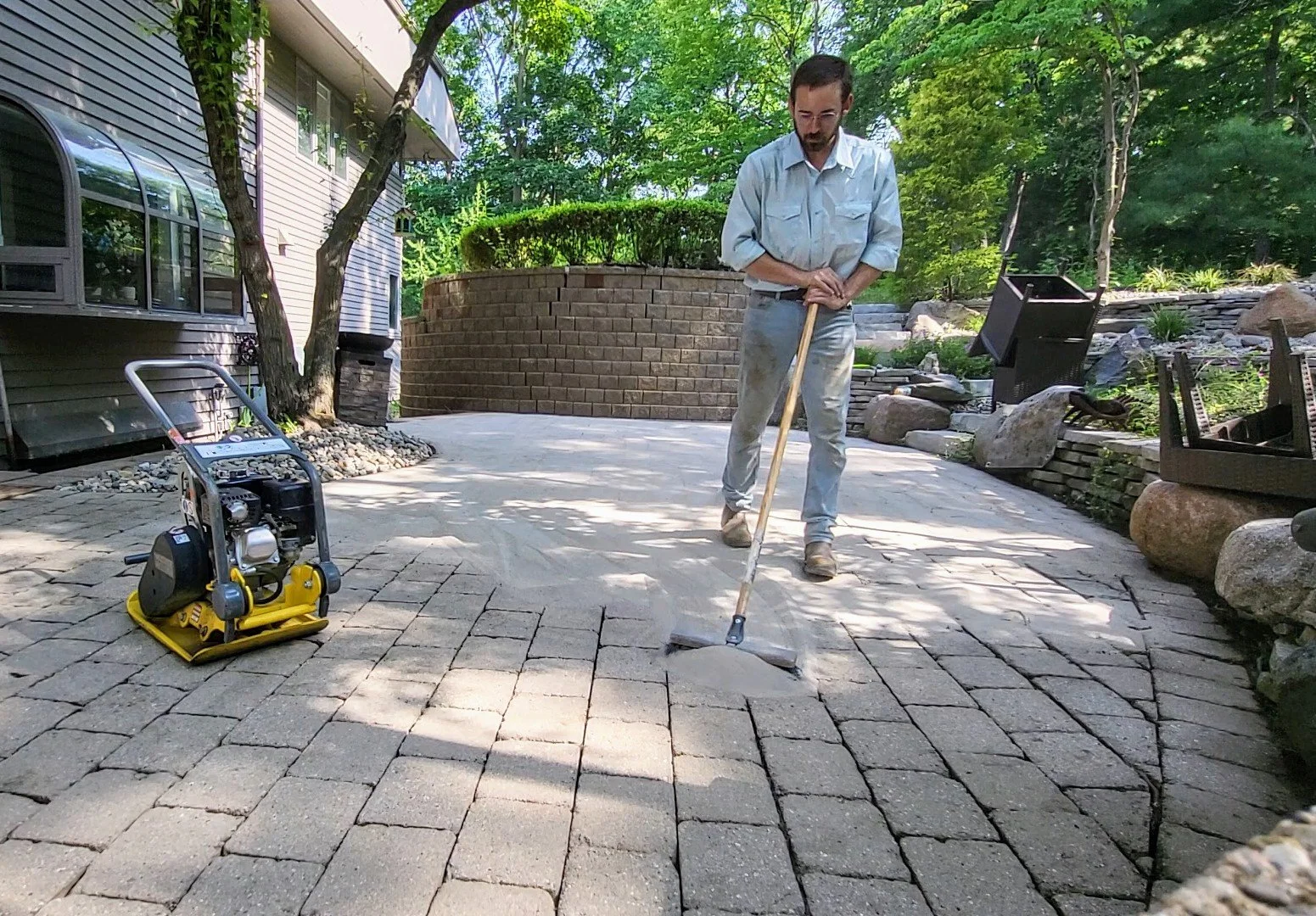 summer photo of gardener brushing sand into paving stones