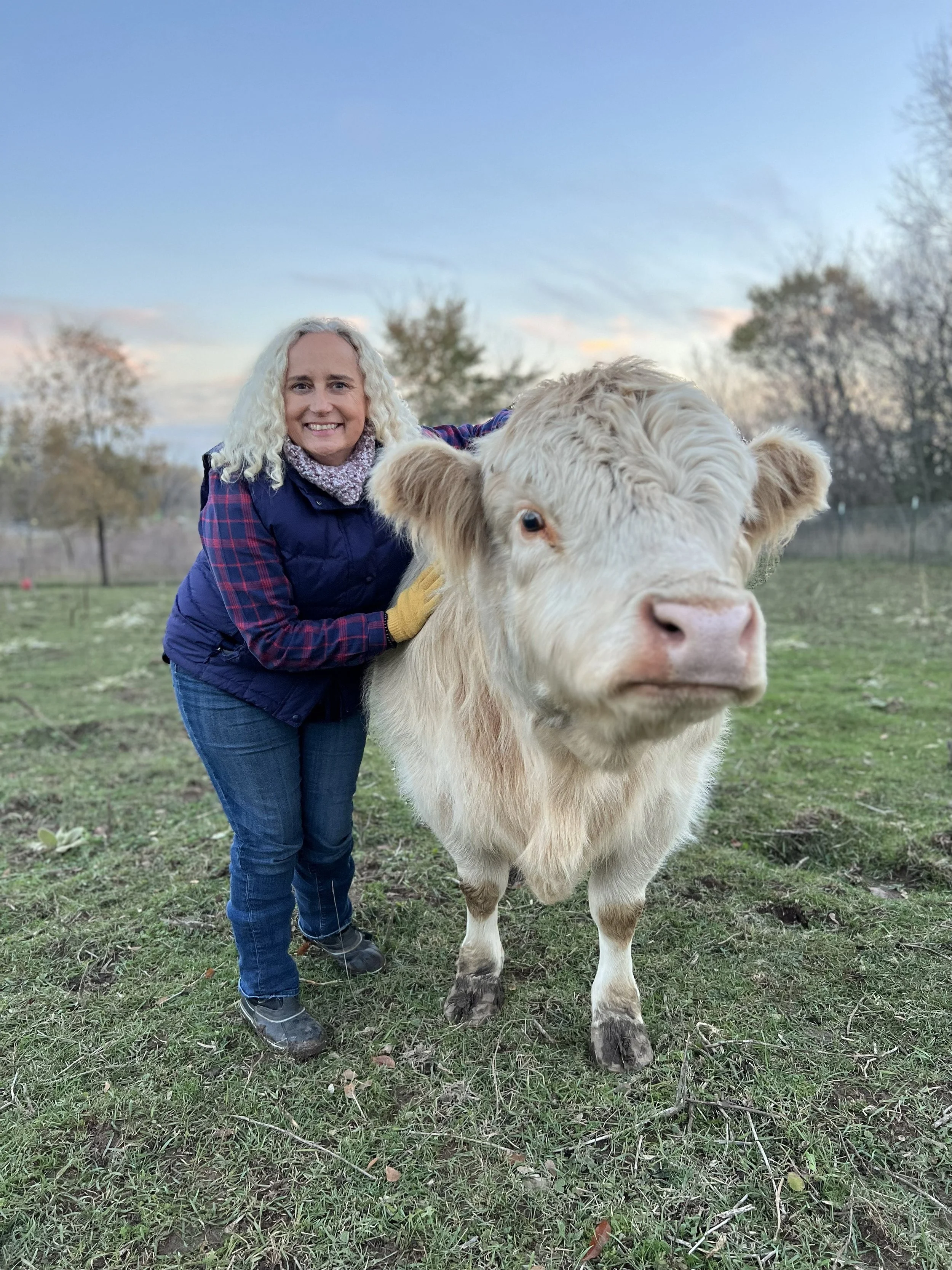 A woman smiling while holding a black and white rooster outdoors with a cloudy sky and green field in the background.