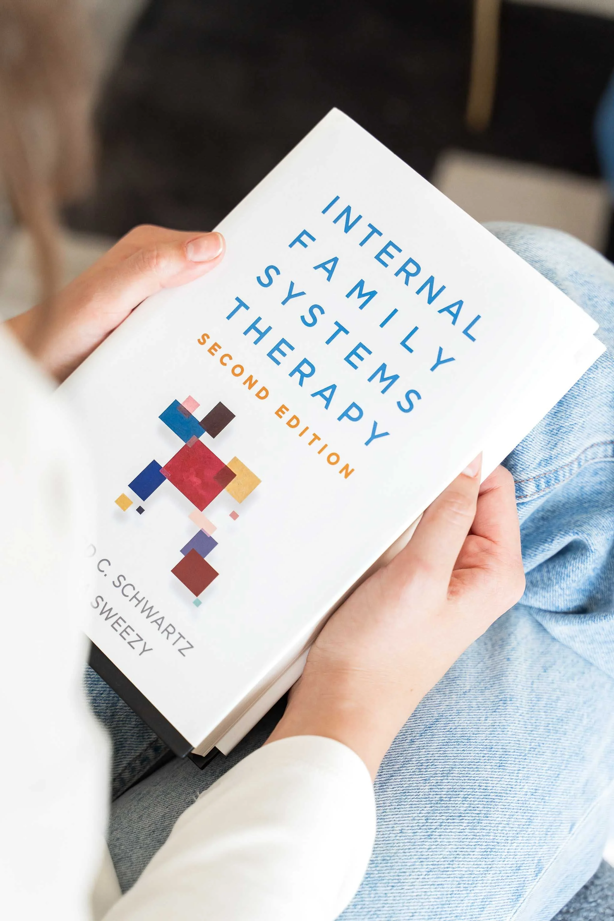 Person holding the Internal Family Systems Therapy book during a family-of-origin healing session in Calgary.