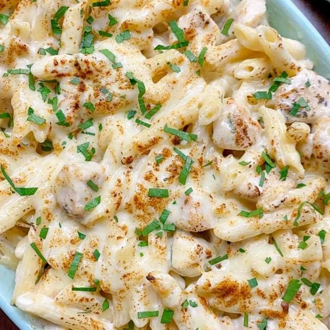 Bowl of creamy macaroni and cheese topped with chopped herbs and paprika.