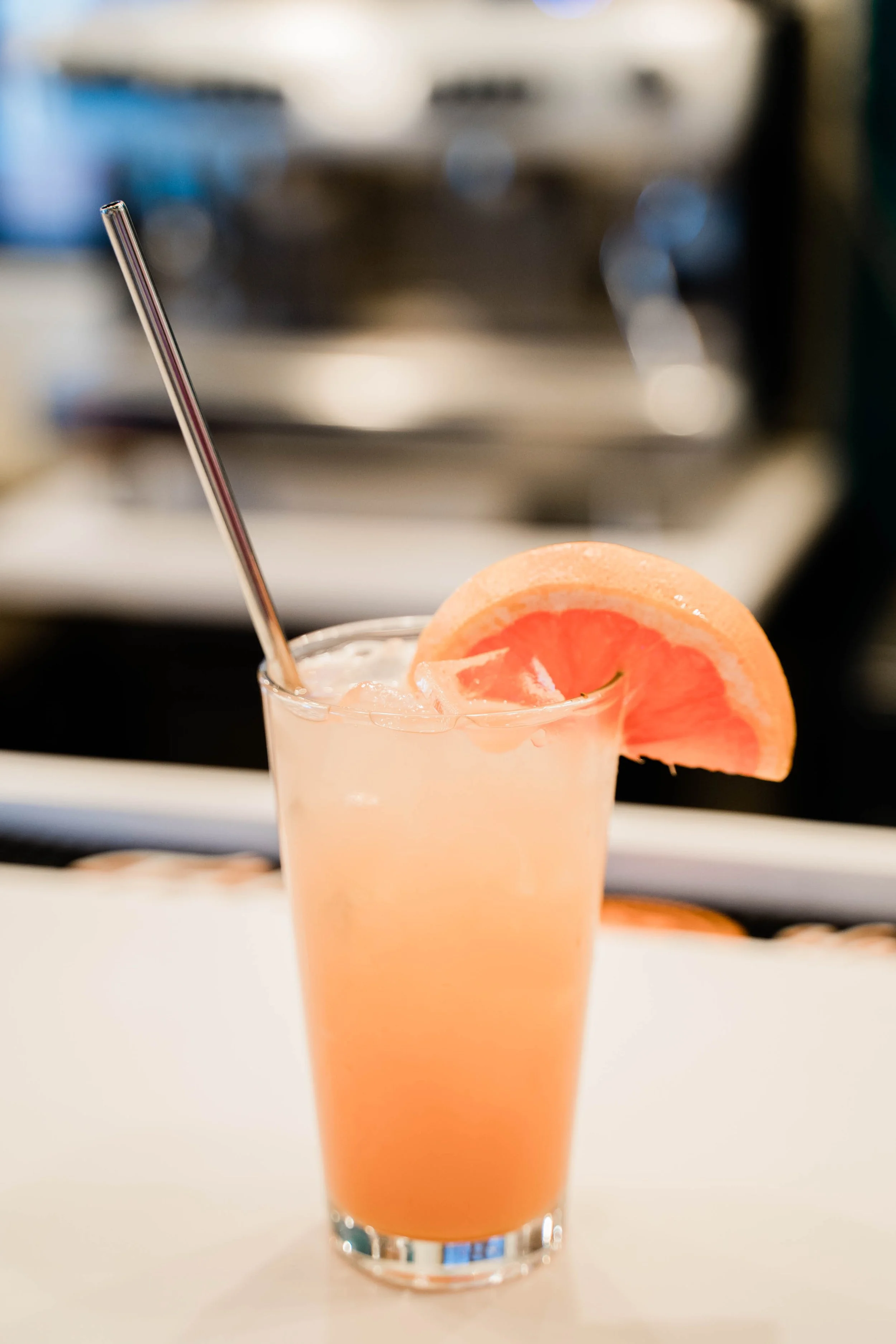 Tall glass of pink grapefruit juice with ice, garnished with a slice of grapefruit and a metal straw.