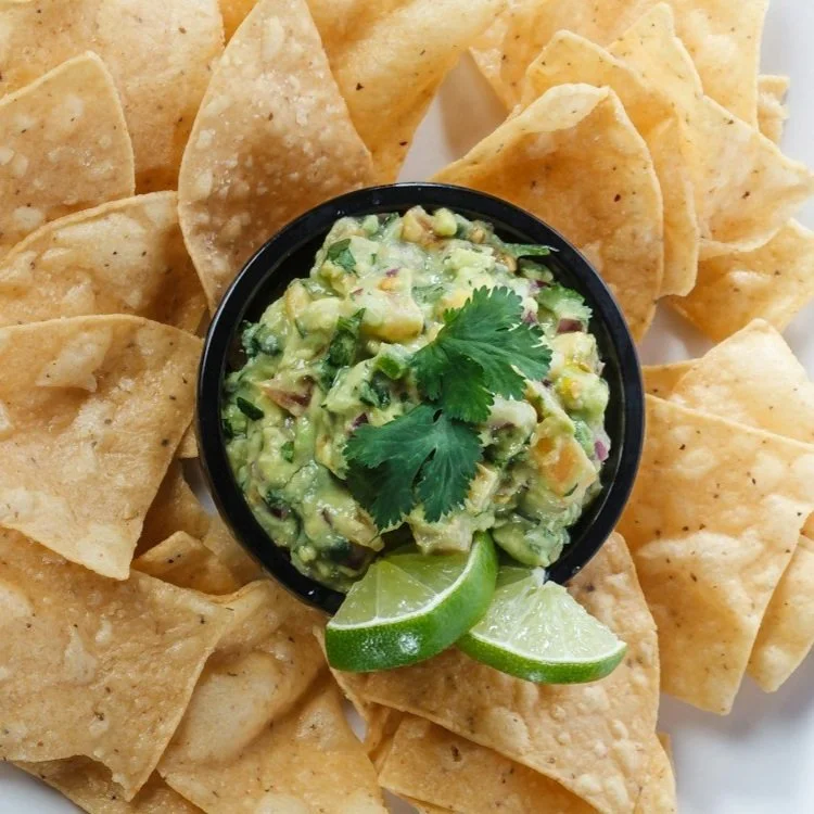 Tortilla chips with a bowl of guacamole and lime wedges.