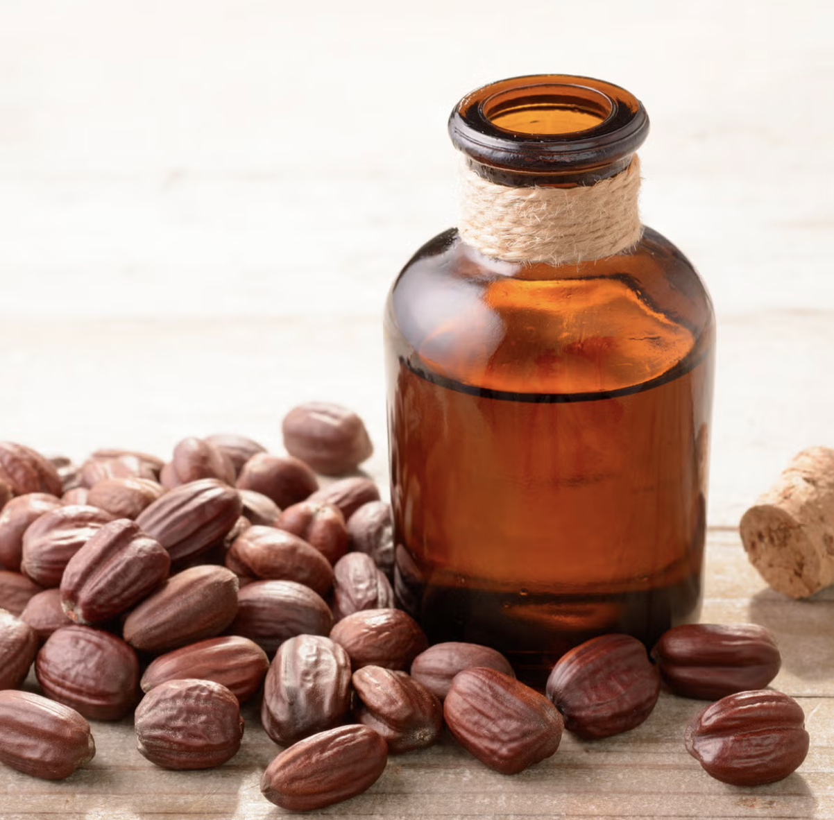 Amber glass bottle with a twine band around its neck, surrounded by scattered raw vanilla beans and a small piece of ginger on a white wooden surface.