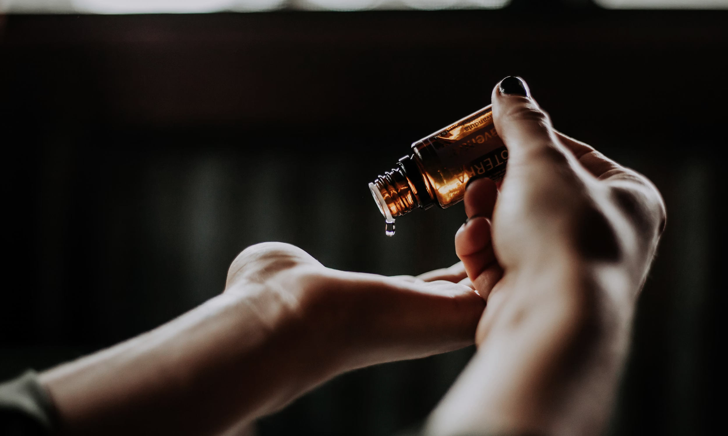 A person's hands holding a small amber-glass bottle, with liquid pouring out of it.