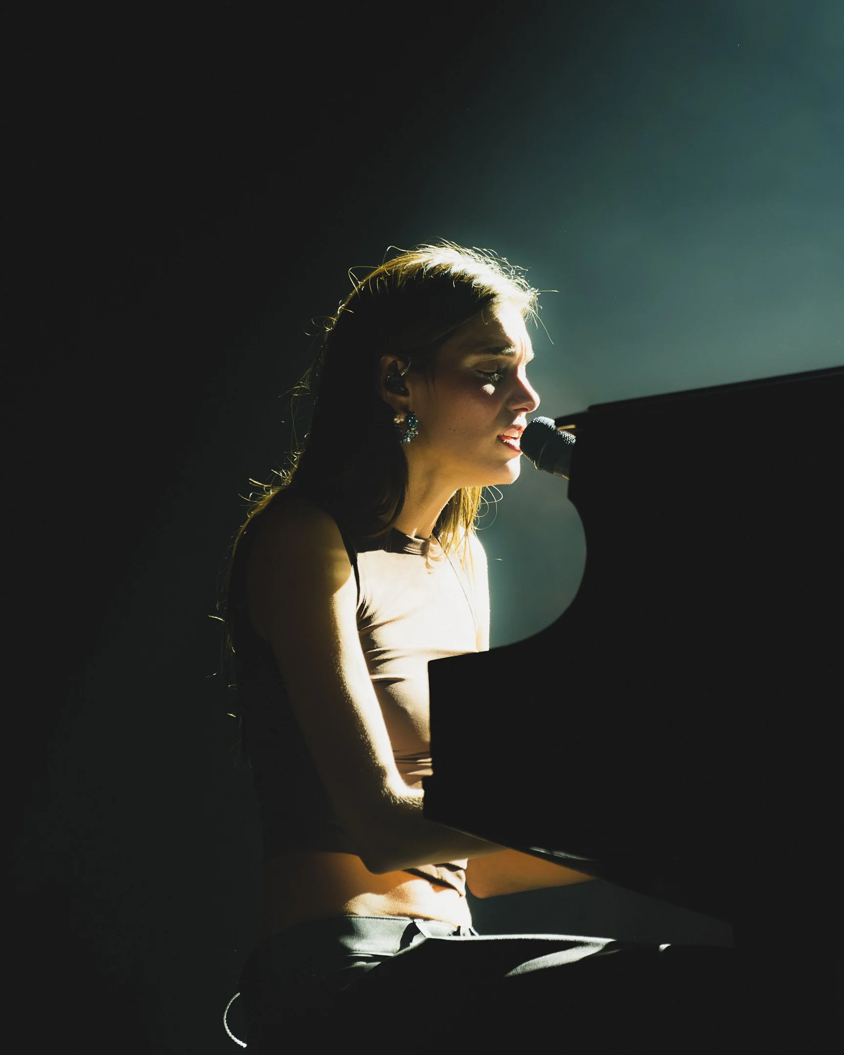 Une personne sur scène jouant du piano et chantant dans un micro, éclairée par un projecteur.