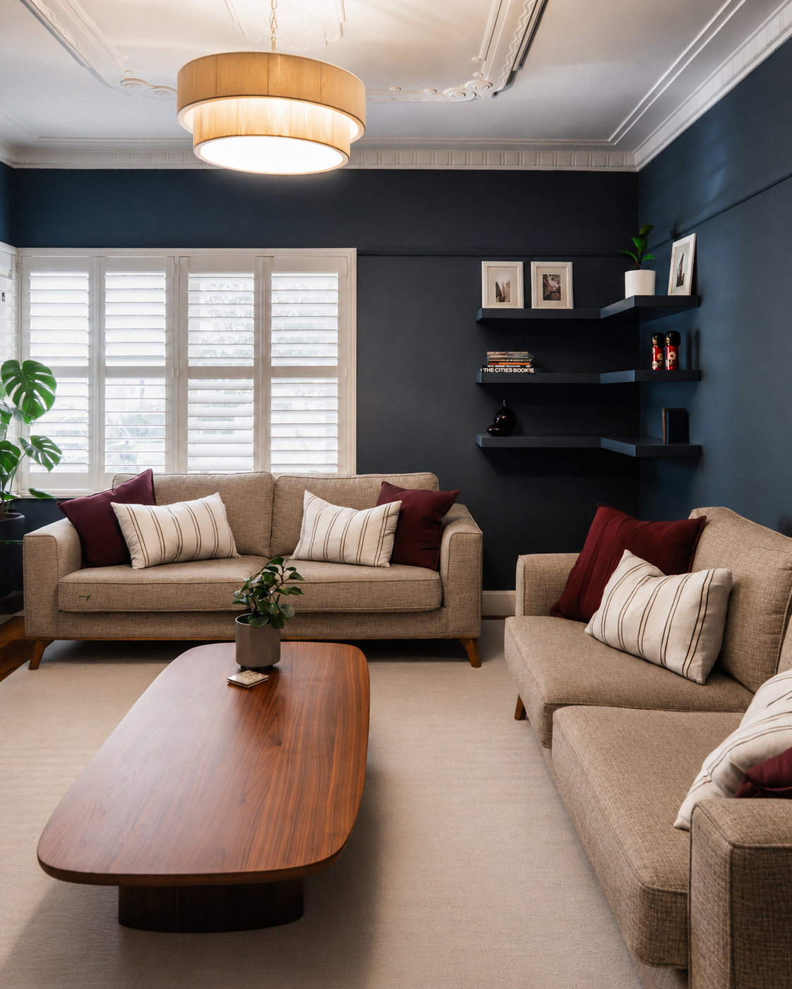 Navy blue lounge room with original ceiling rose, plantation shutters and floating corner shelving, Yarraville renovation by Lúrae Studio
