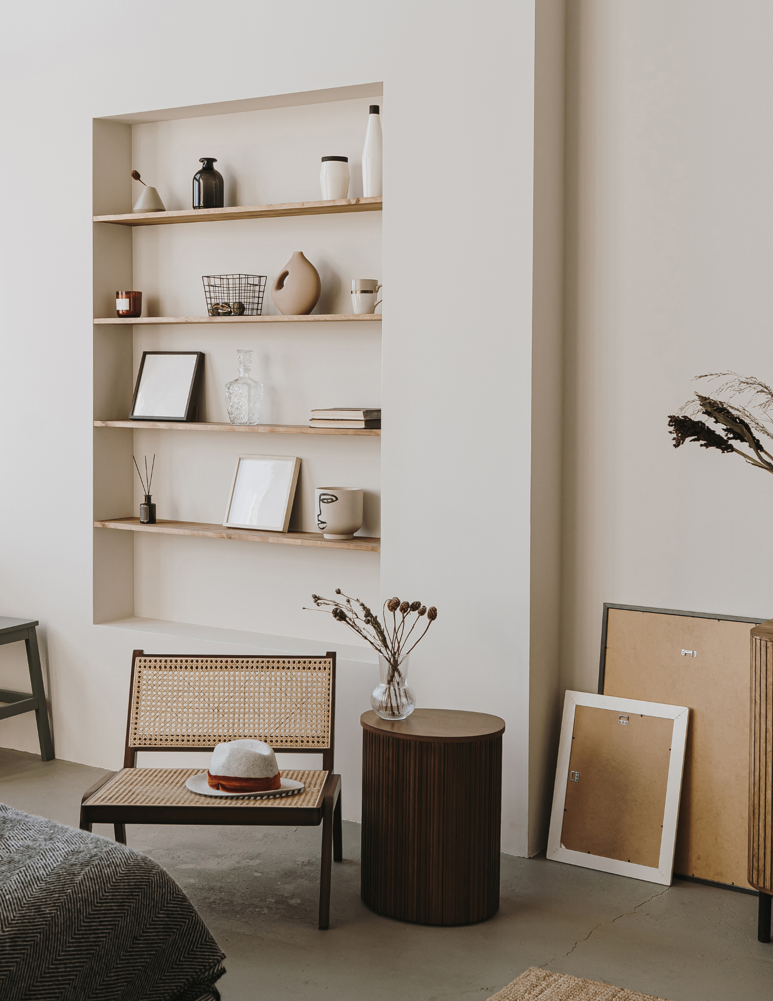 Minimalist living room with built-in shelves, decorative items, a cane chair with a hat, a small round table, and framed artwork.