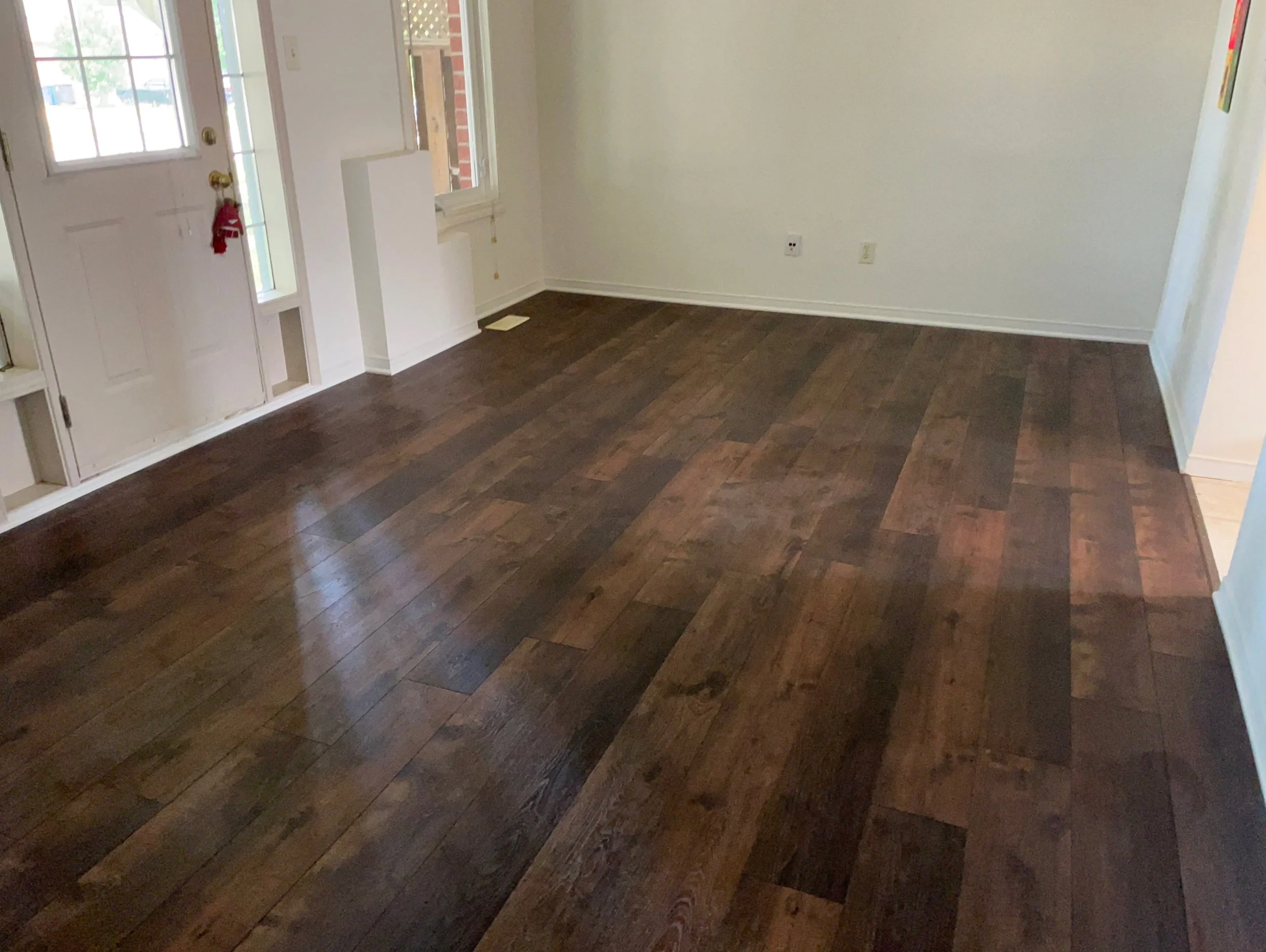 Empty room with dark laminate flooring, white walls, front door with a window, and several windows on the side wall, with some Christmas decorations hanging on the door handles.