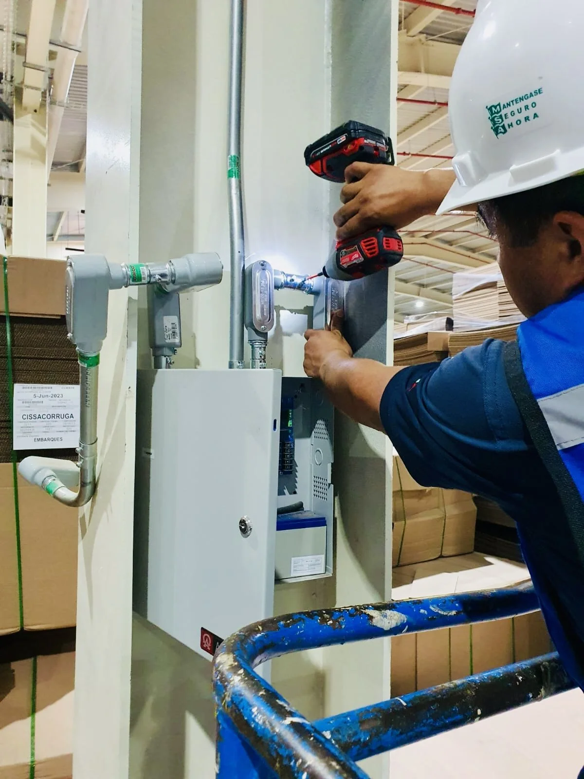 Un trabajador instalando o reparando un sistema de plomería con herramientas eléctricas en una estructura metálica en un almacén o tienda de madera.