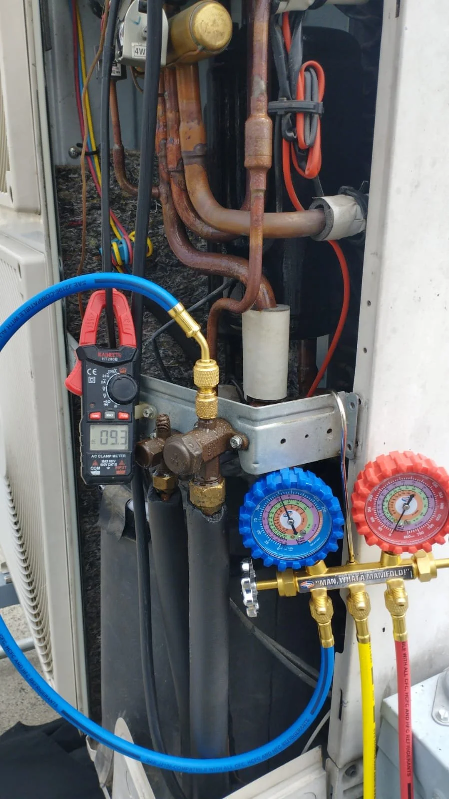 Componentes internos de un aire acondicionado, incluyendo tubos de cobre, medidor de presión y ferramentas de diagnóstico.