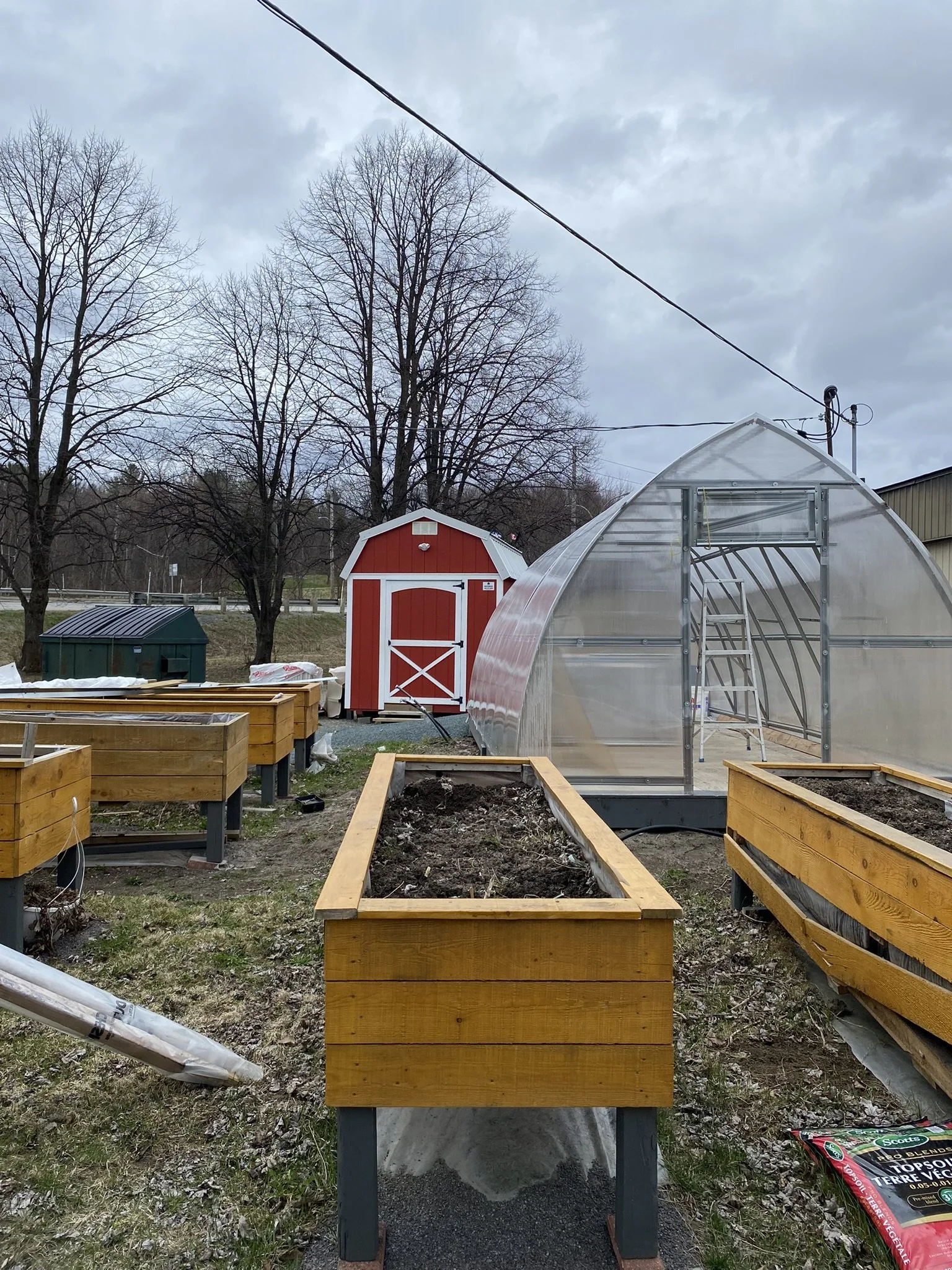 jardin sur pied dans des bacs de bois à l'extérieur avec une serre et une remise