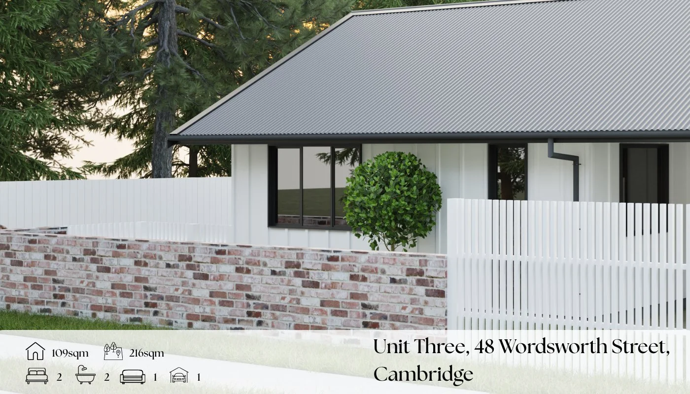 Front view of a modern house with a sloped metal roof, white vertical siding, and black window frames. There is a green tree and a brick wall in front of the house, and a white picket fence.