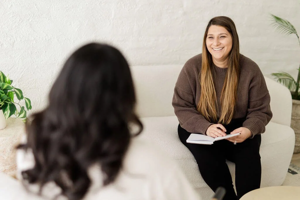 best therapists mission viejo woman brown hair brown sweater black pants notebook in hand sitting across from client smiling
