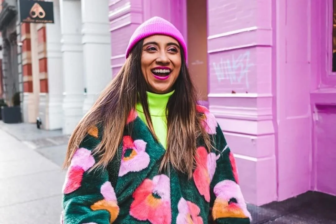 counseling for bipoc orange county woman smiling long hair hot pink beanie highlighter yellow shirt bright floral pattern jacket
