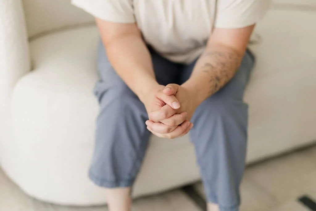 anxiety therapist orange county person sitting on white couch with blue pants holding hands leaning forward