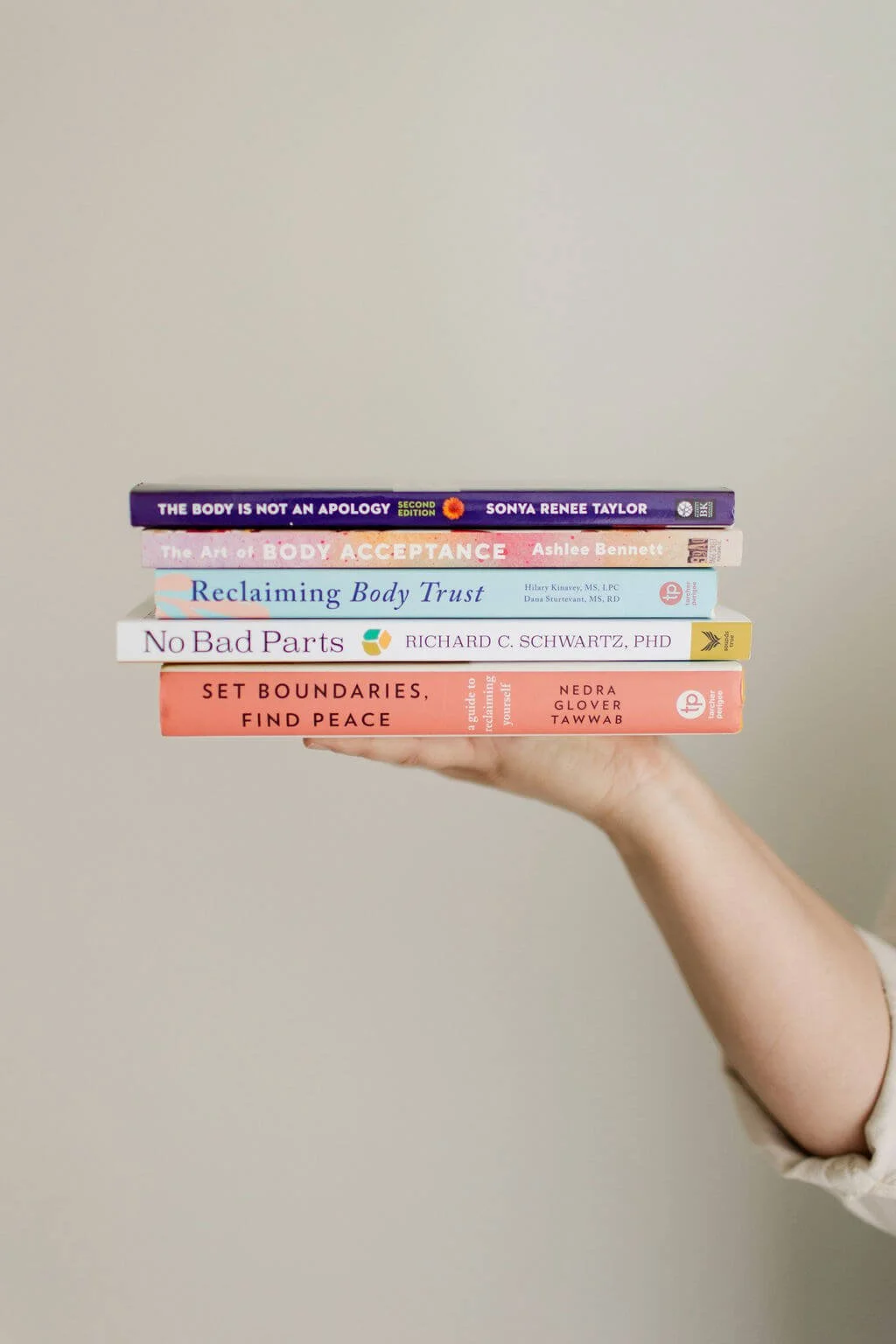 eating disorder therapy orange county hand holding stack of books including the body is not an apology, art of body acceptance, reclaiming body trust, no bad parts, and set boundaries, find peace