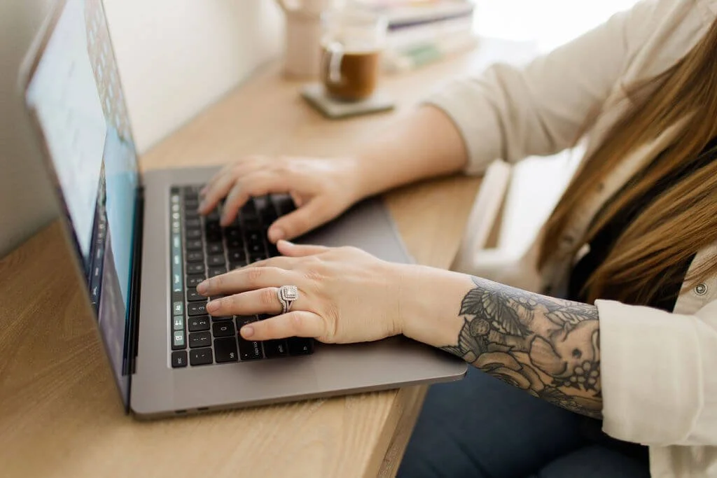 counselor in mission viejo hands typing on laptop tattooed arm coffee and books in background