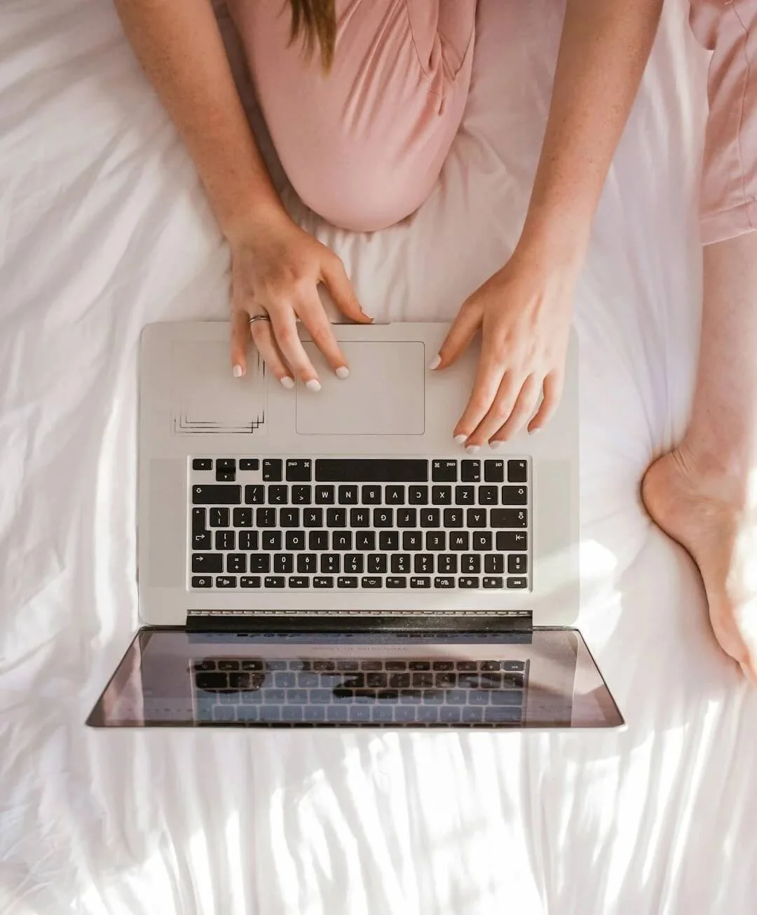 online therapy ohio person sitting on bed wearing pink sweatpants using silver laptop with black keyboard