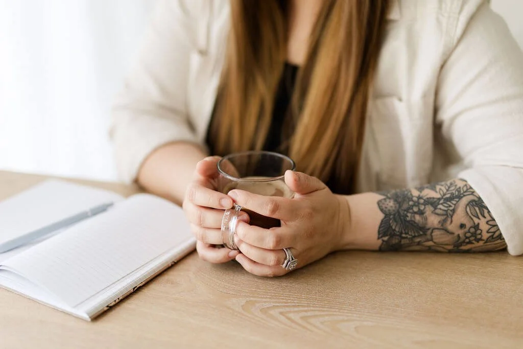 trauma therapist orange county hands cupping coffee left forearm tattoo notebook open on table