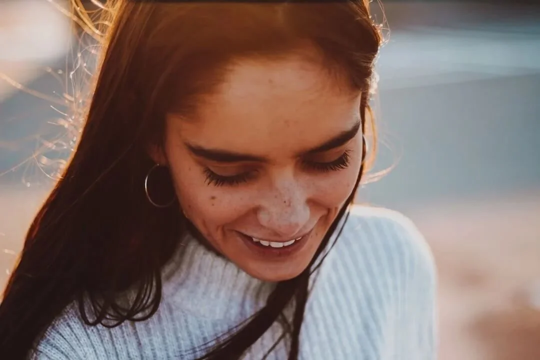 trauma therapist orange county women brown hair hoop earrings smiling glancing down wearing gray turtle neck sweater sunset orange outlining her hair