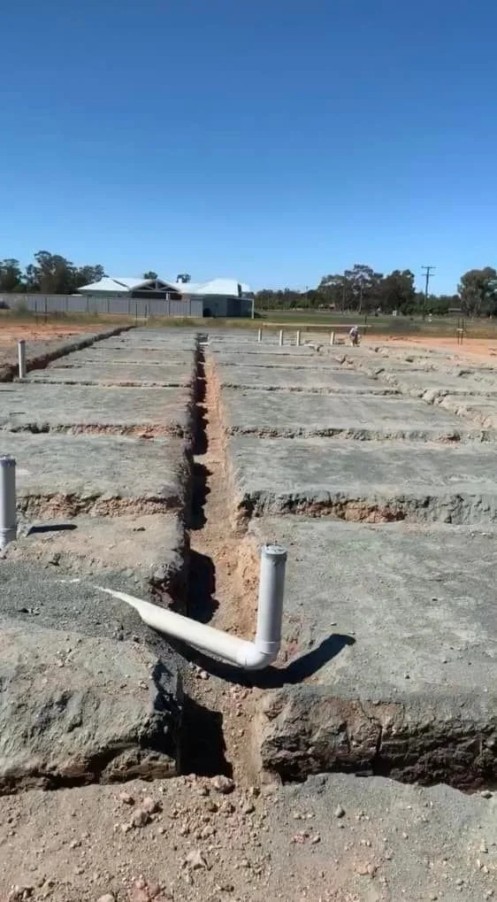 Multiple concrete building foundations with PVC pipes in a construction site under a clear blue sky.