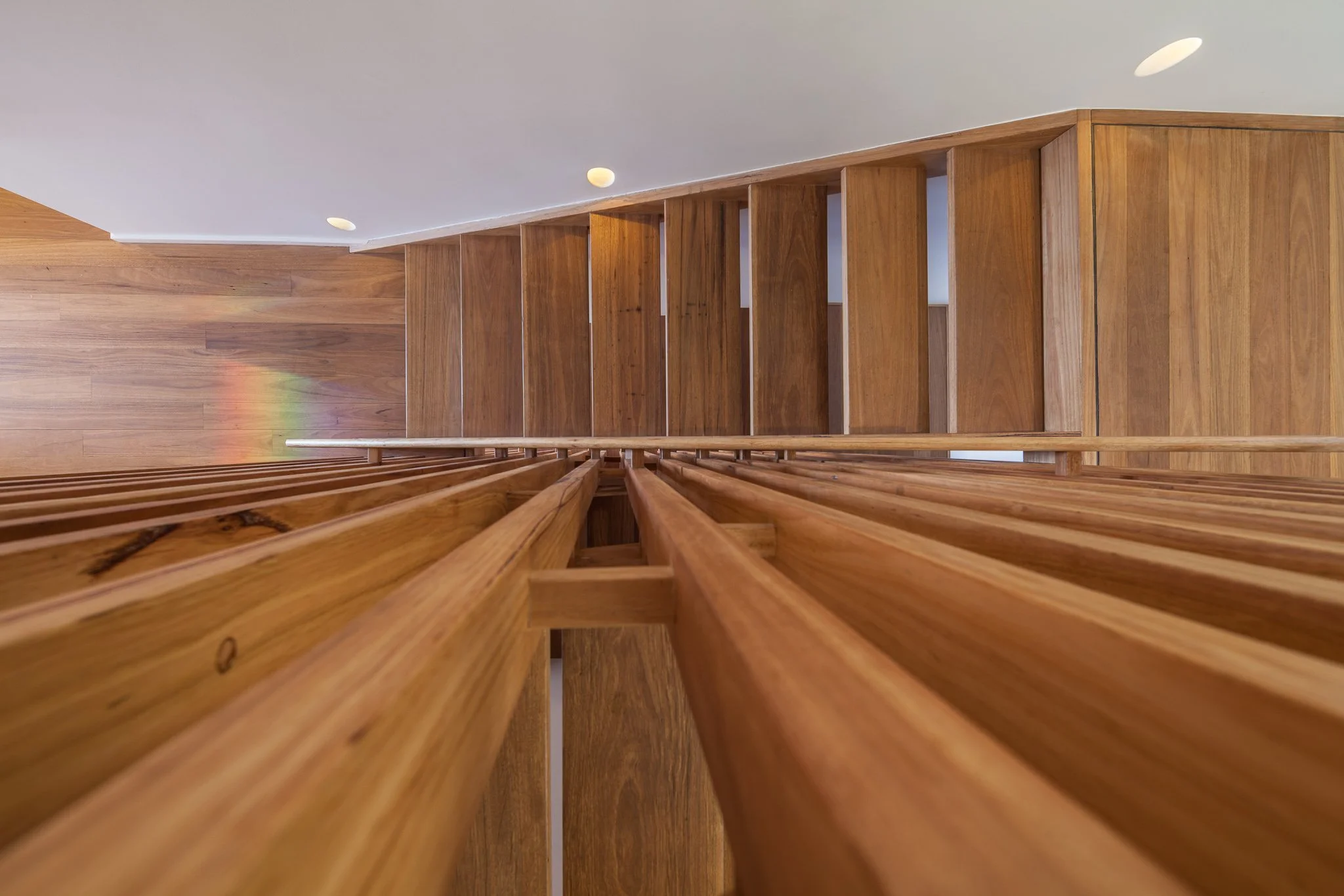 View of a wooden staircase from above, showing the steps and handrail with a white wall and ceiling with recessed lights in the background.