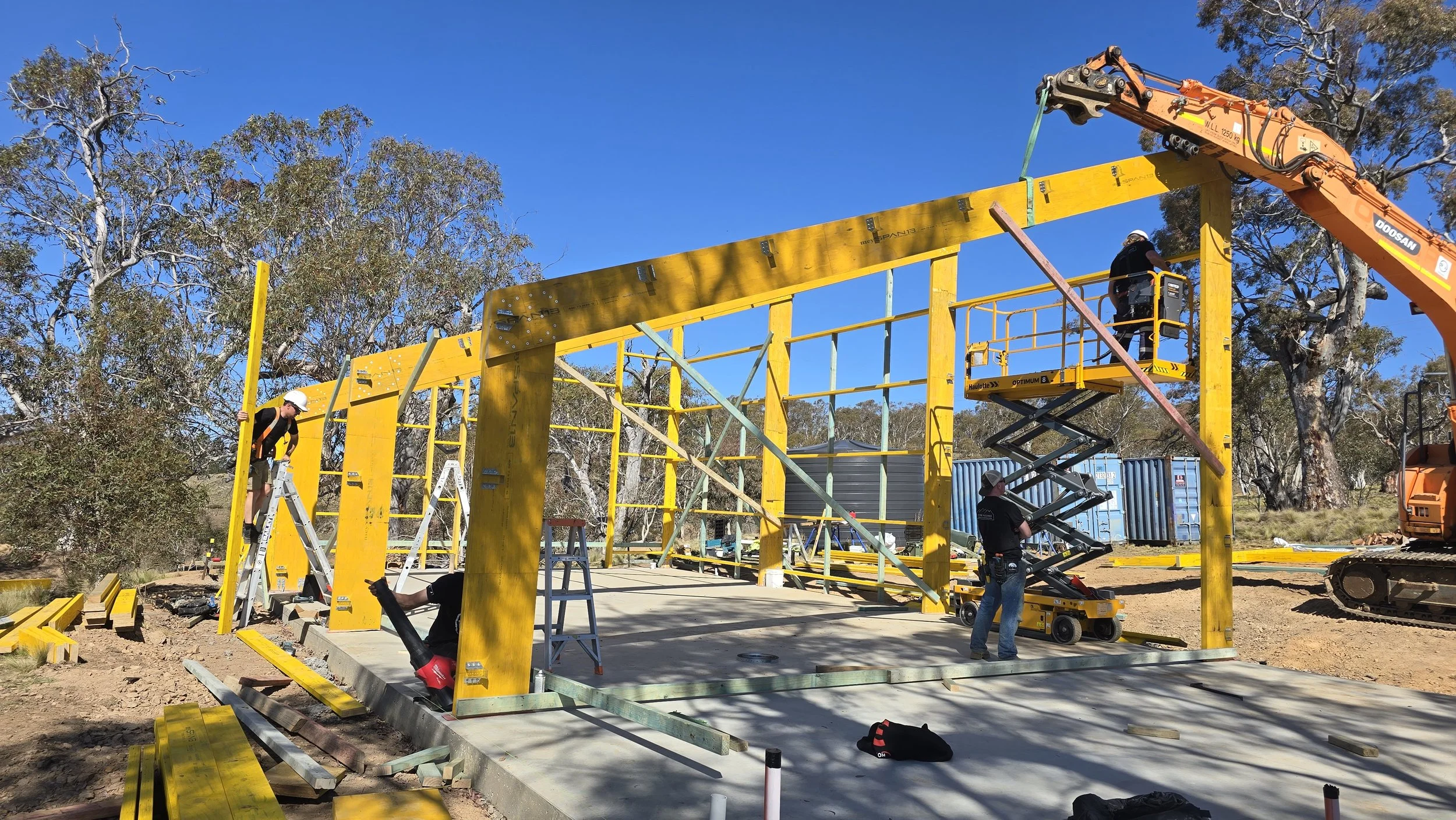 Alpine PassivHaus crew raising timber portal frames with crane and scissor lift