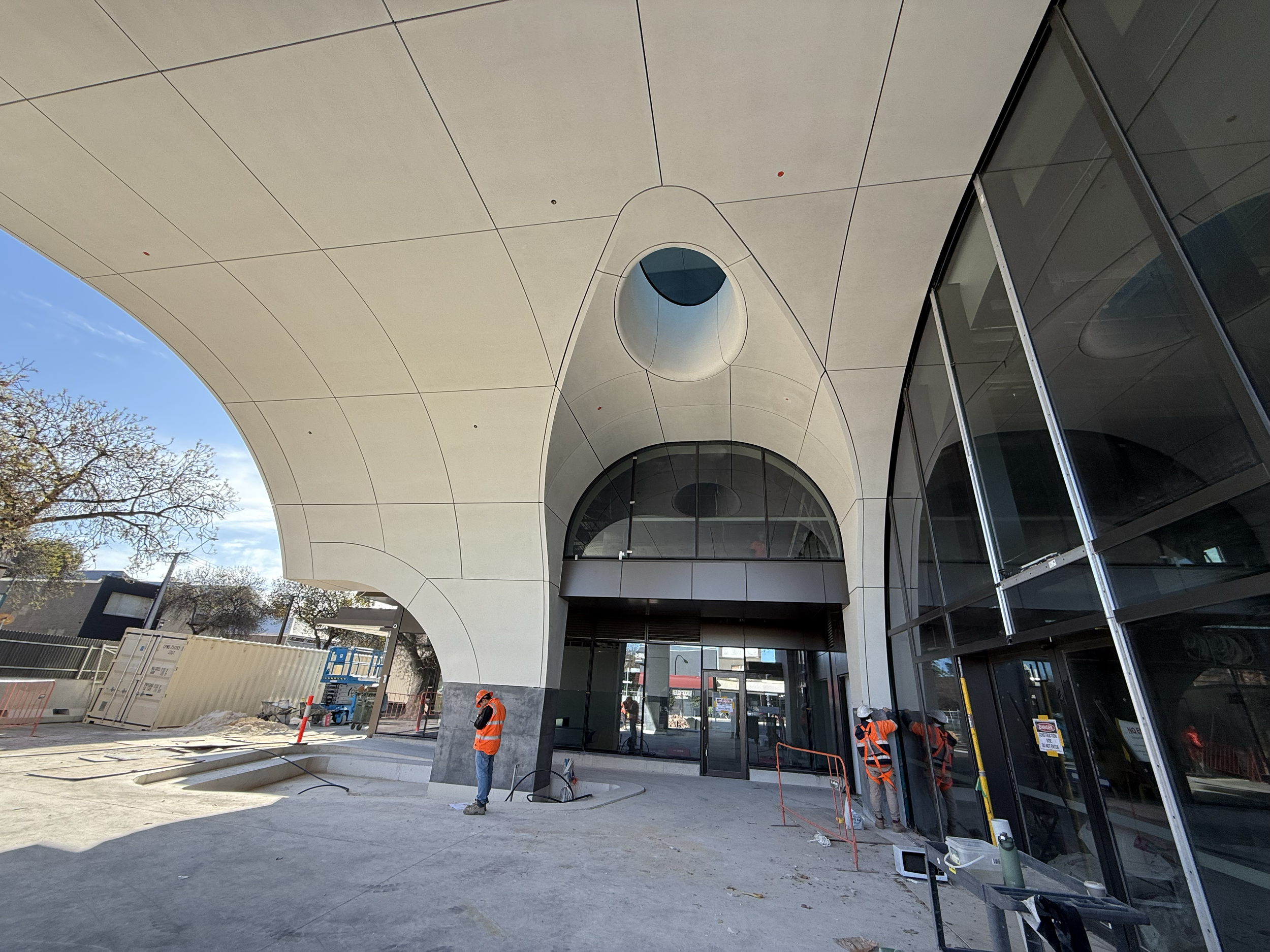 Construction workers in safety vests working outside a modern building with a curved white roof and glass walls.